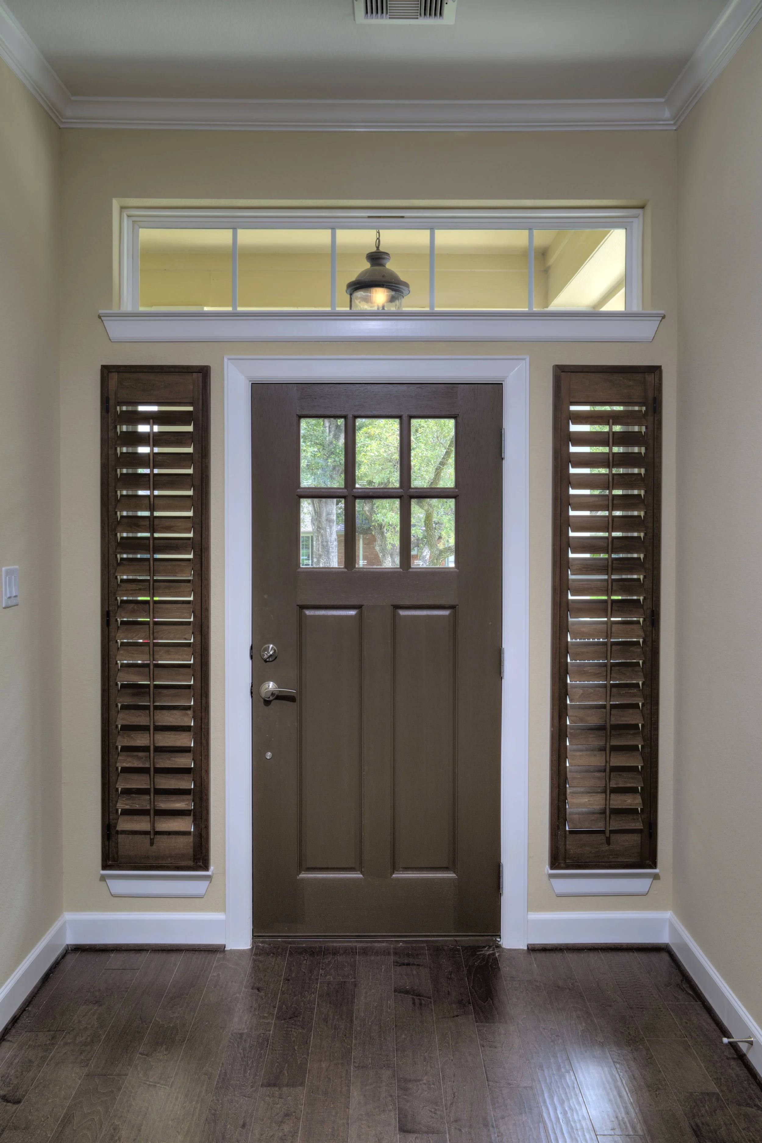 Custom dark stained shutters with classic tilt rods on sidelights beside the front door of a Houston, Texas home.