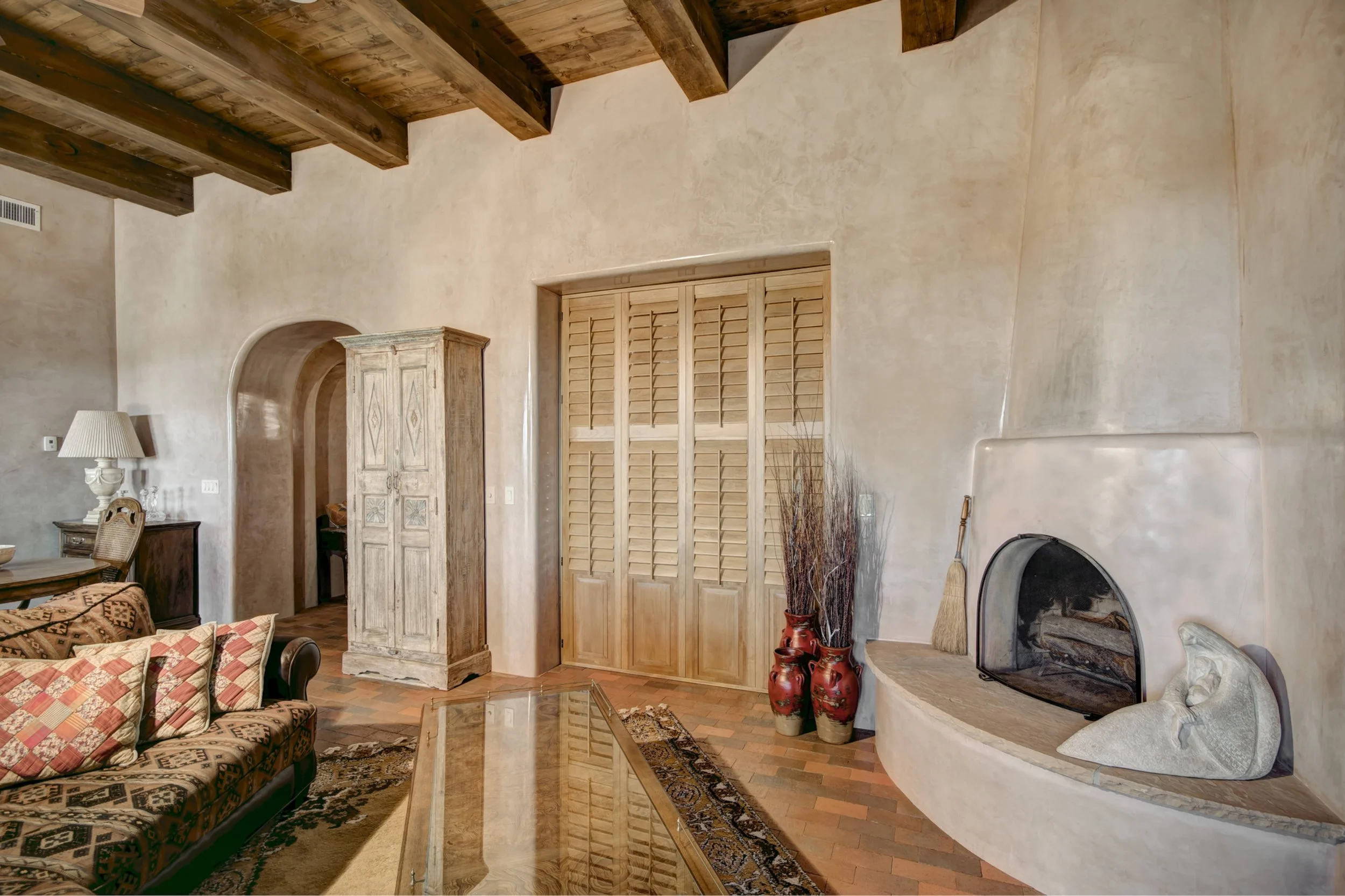 Custom Sands-stained hardwood shutters set into a deep plaster opening beside a kiva fireplace in Santa Fe, New Mexico.