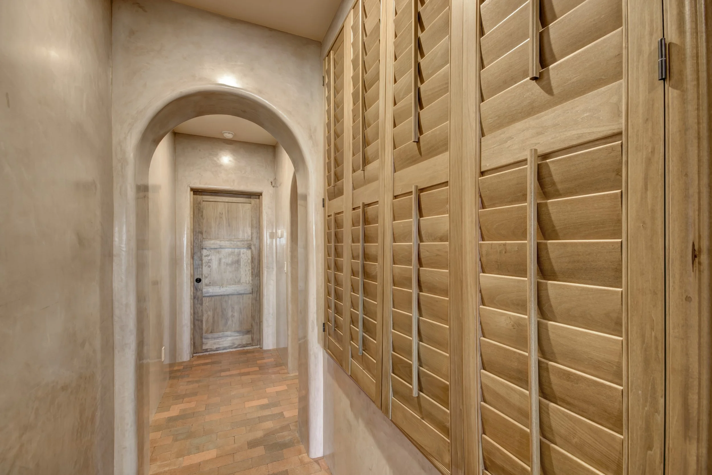 Sands-stained hardwood shutters line an arched plaster hallway in a Santa Fe, New Mexico home.