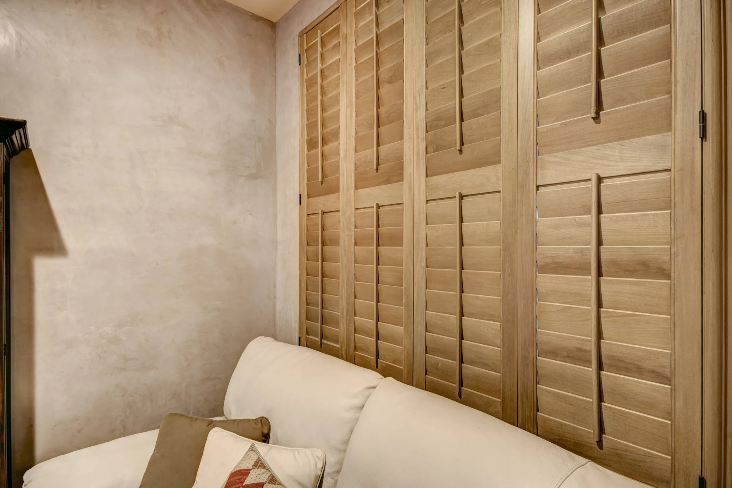 Sands-stained hardwood shutters frame an interior window opening beside a rounded archway in a Santa Fe home.
