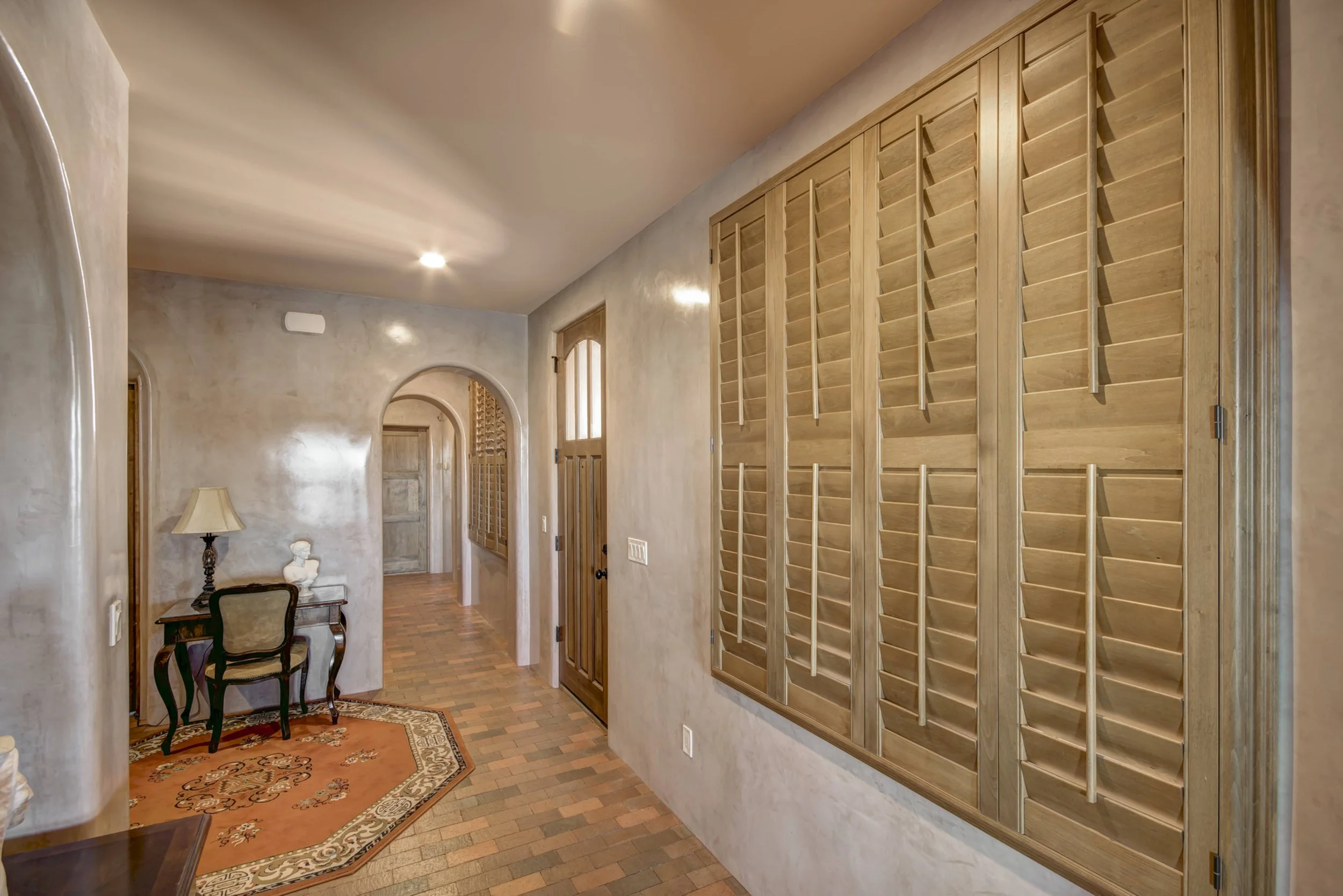 Large Sands-stained hardwood shutters bring warmth to a plaster-walled hallway in a Santa Fe, New Mexico home.