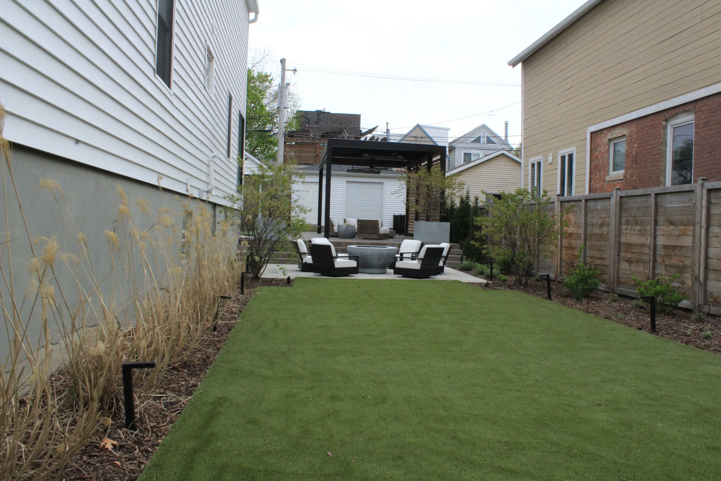 This custom space embraced two levels of patio and yard space, a custom louvered aluminum pergola complete with heater, lights, and fans, an outdoor fire pit, synthetic turf lawn for the pups and kids to play on, custom lighting system, and irrigatio
