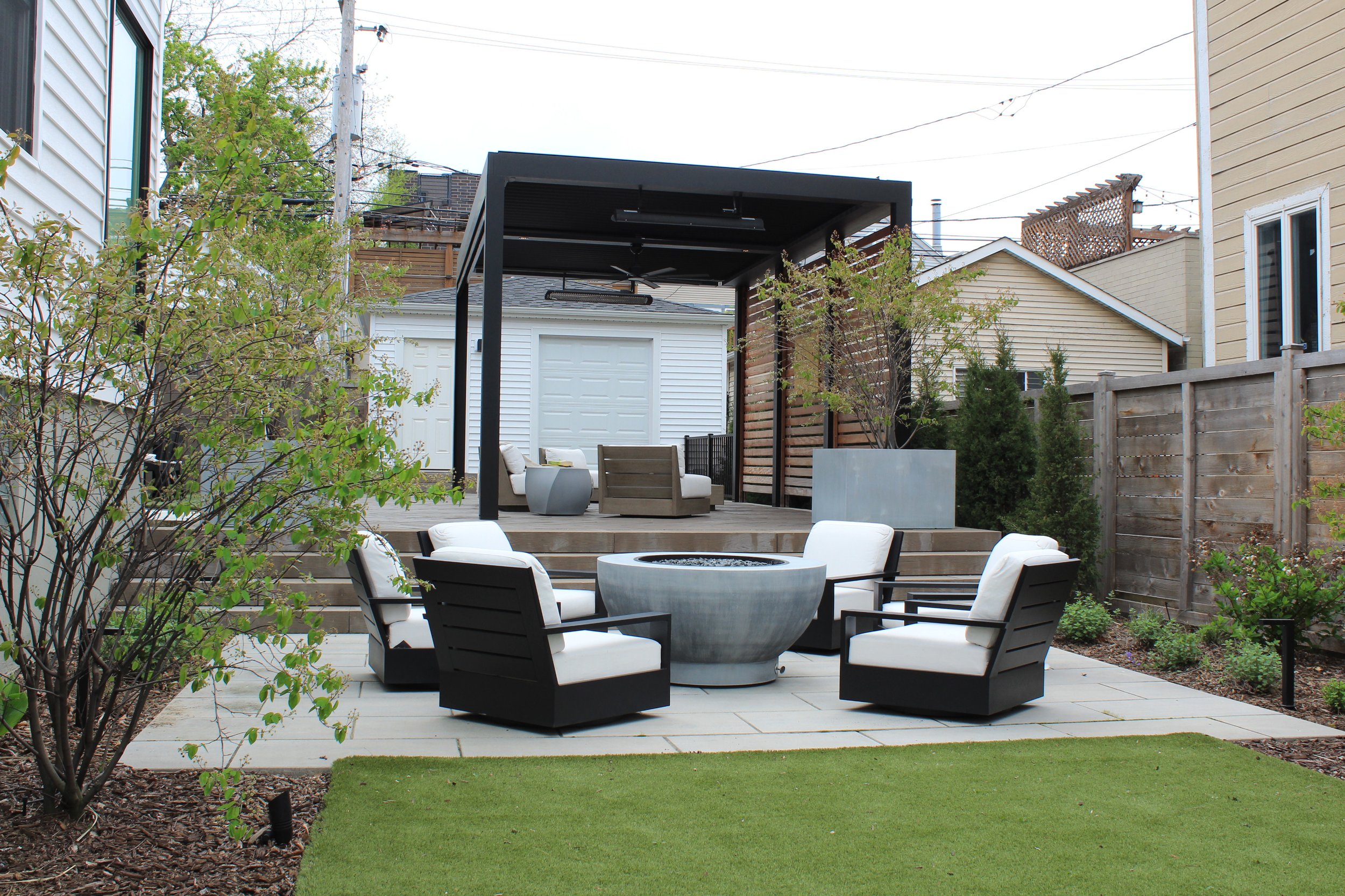 This custom space embraced two levels of patio and yard space, a custom louvered aluminum pergola complete with heater, lights, and fans, an outdoor fire pit, synthetic turf lawn for the pups and kids to play on, custom lighting system, and irrigatio