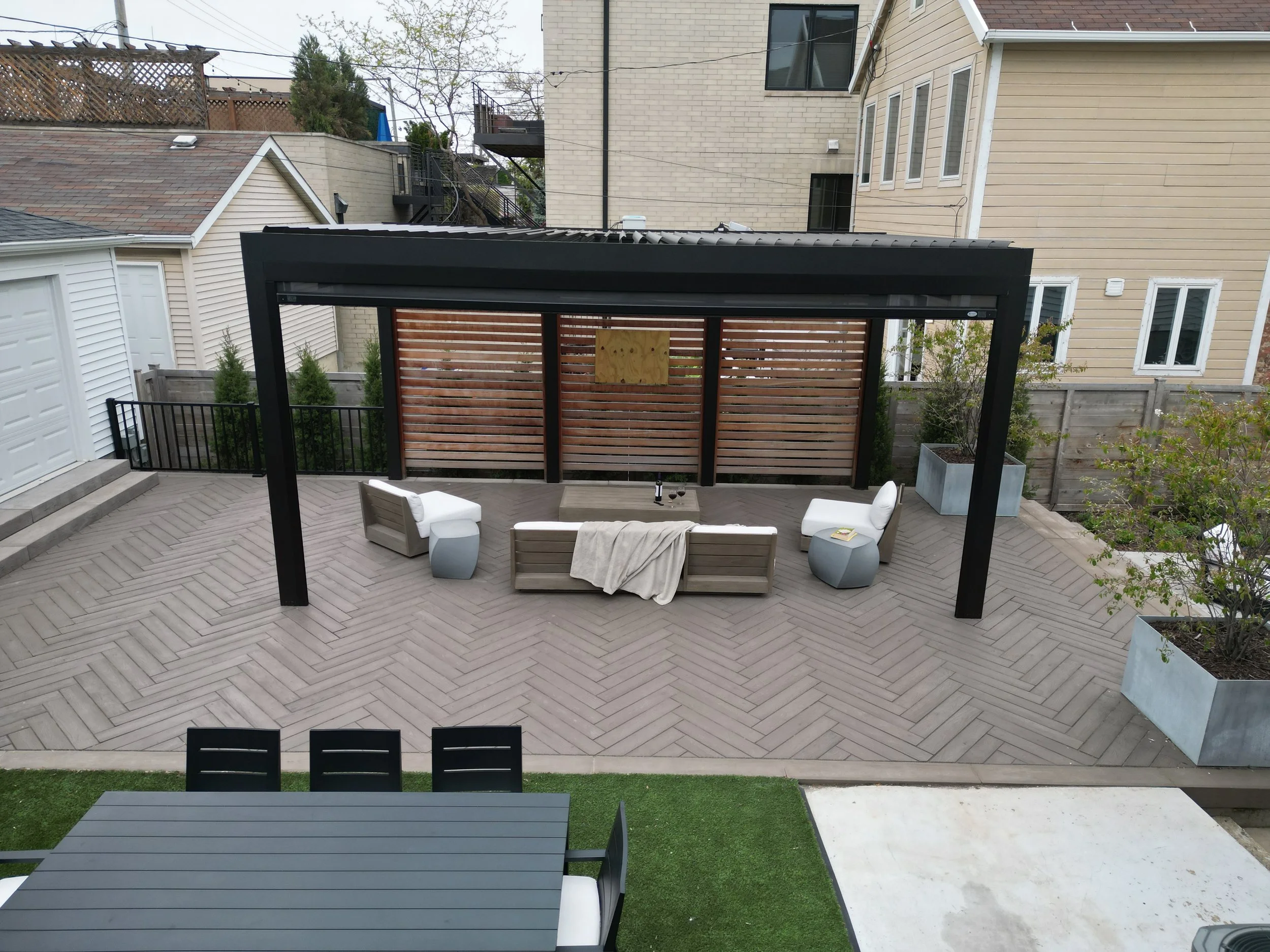 This custom space embraced two levels of patio and yard space, a custom louvered aluminum pergola complete with heater, lights, and fans, an outdoor fire pit, synthetic turf lawn for the pups and kids to play on, custom lighting system, and irrigatio