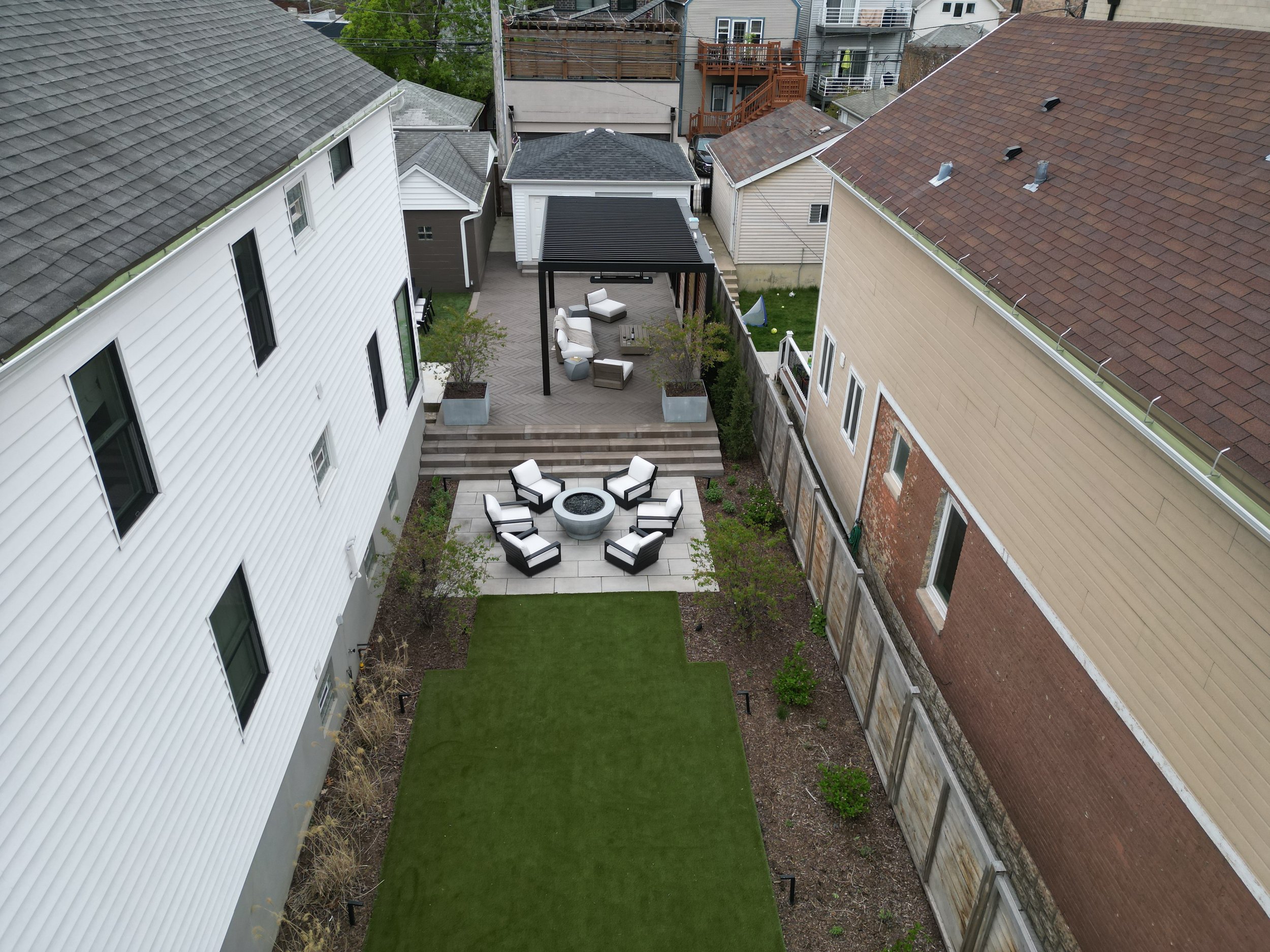This custom space embraced two levels of patio and yard space, a custom louvered aluminum pergola complete with heater, lights, and fans, an outdoor fire pit, synthetic turf lawn for the pups and kids to play on, custom lighting system, and irrigatio