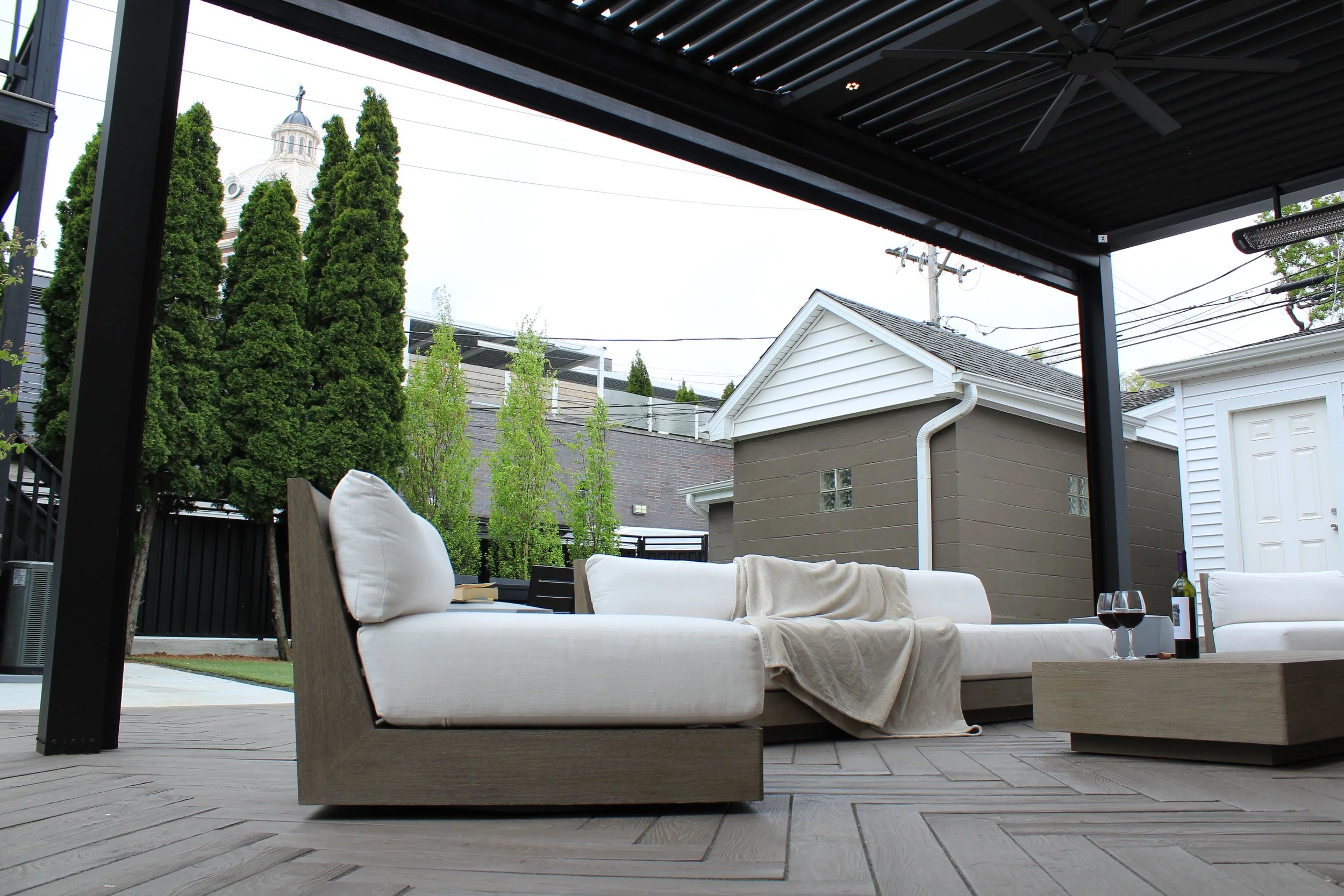 This custom space embraced two levels of patio and yard space, a custom louvered aluminum pergola complete with heater, lights, and fans, an outdoor fire pit, synthetic turf lawn for the pups and kids to play on, custom lighting system, and irrigatio