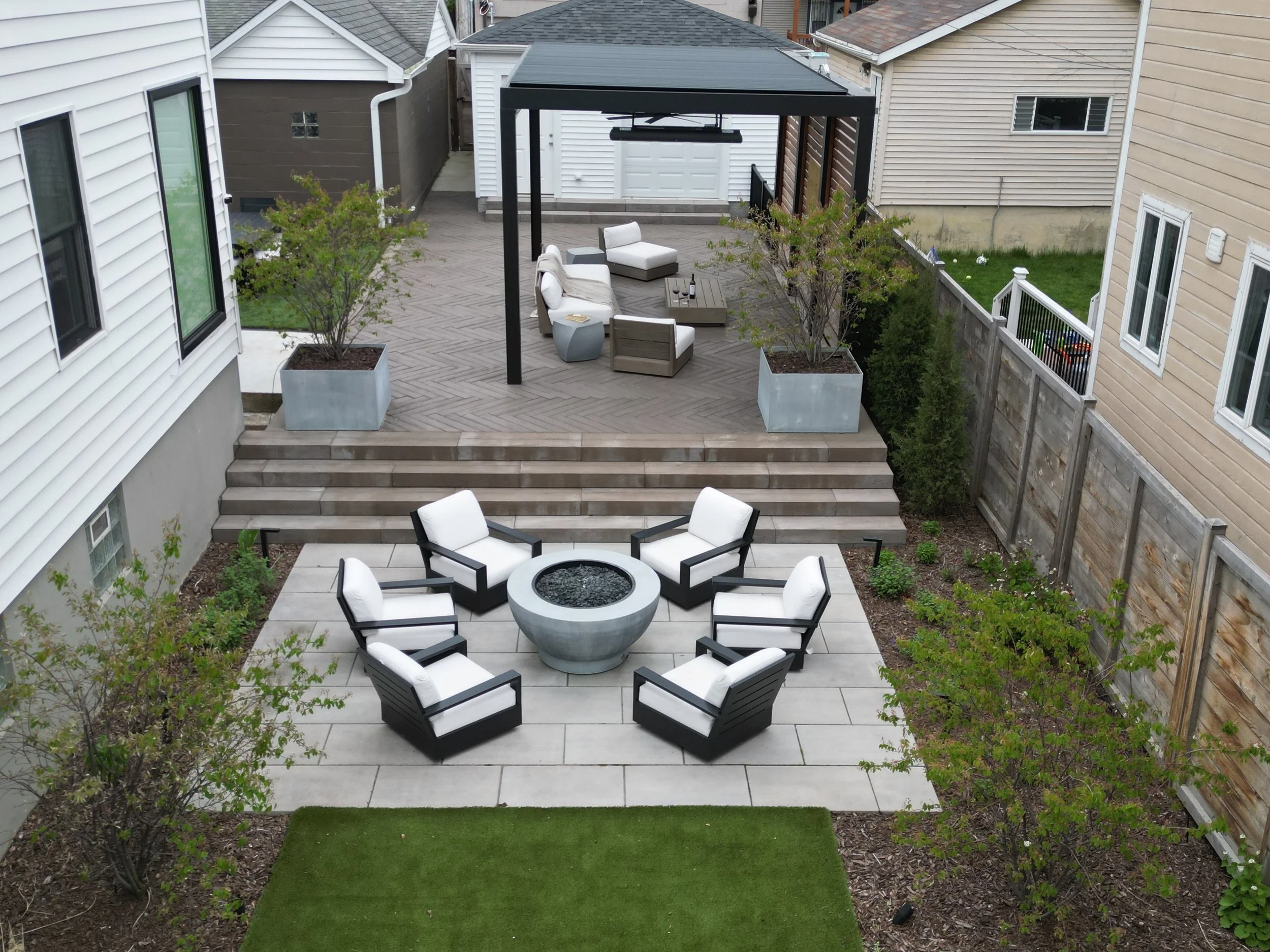 This custom space embraced two levels of patio and yard space, a custom louvered aluminum pergola complete with heater, lights, and fans, an outdoor fire pit, synthetic turf lawn for the pups and kids to play on, custom lighting system, and irrigatio