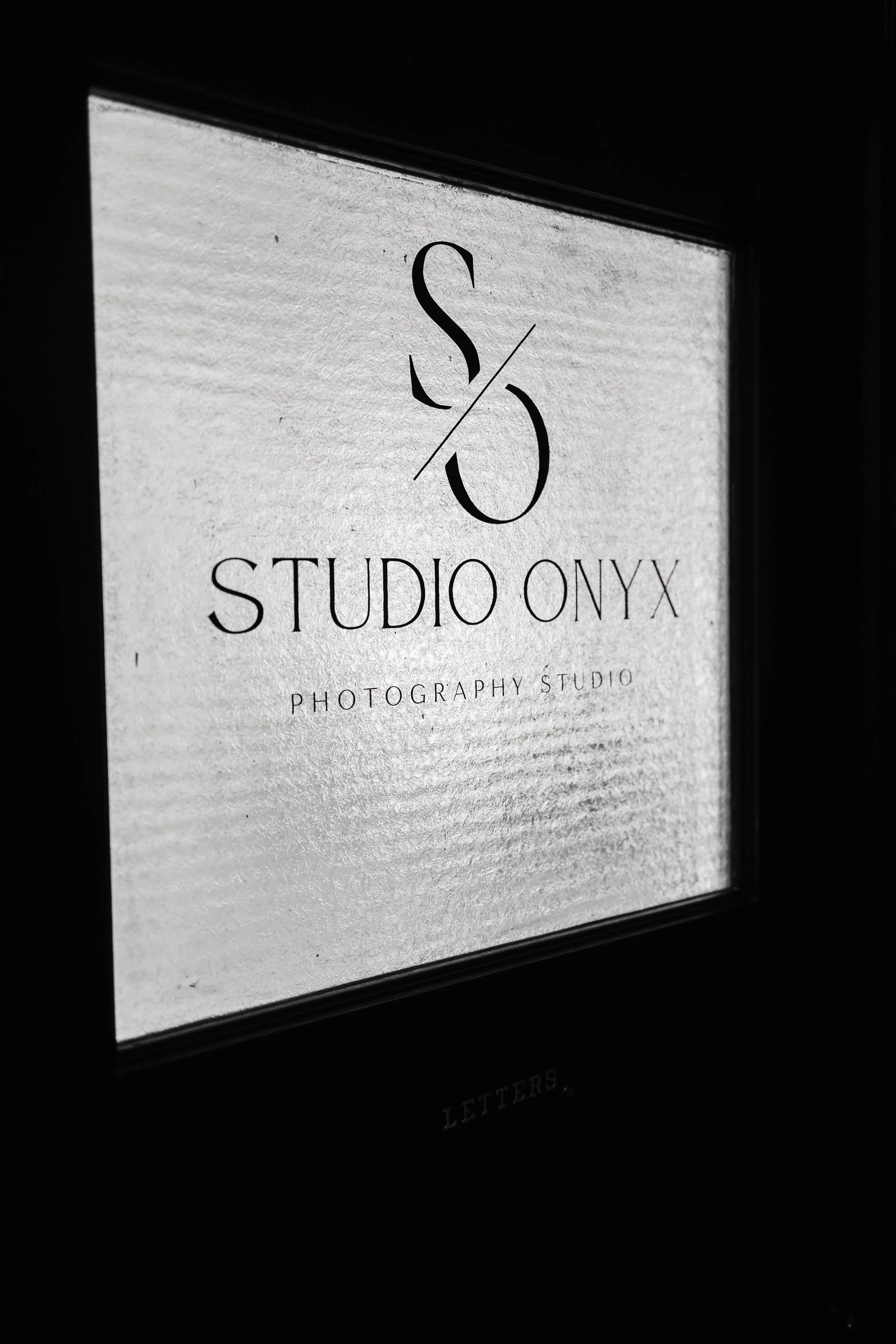 Sign for Studio Onyx Photography Studio with a stylish logo and text, viewed through a textured window or glass with a black border.