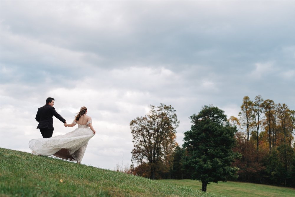 Newly married couple walking together across a grassy hillside