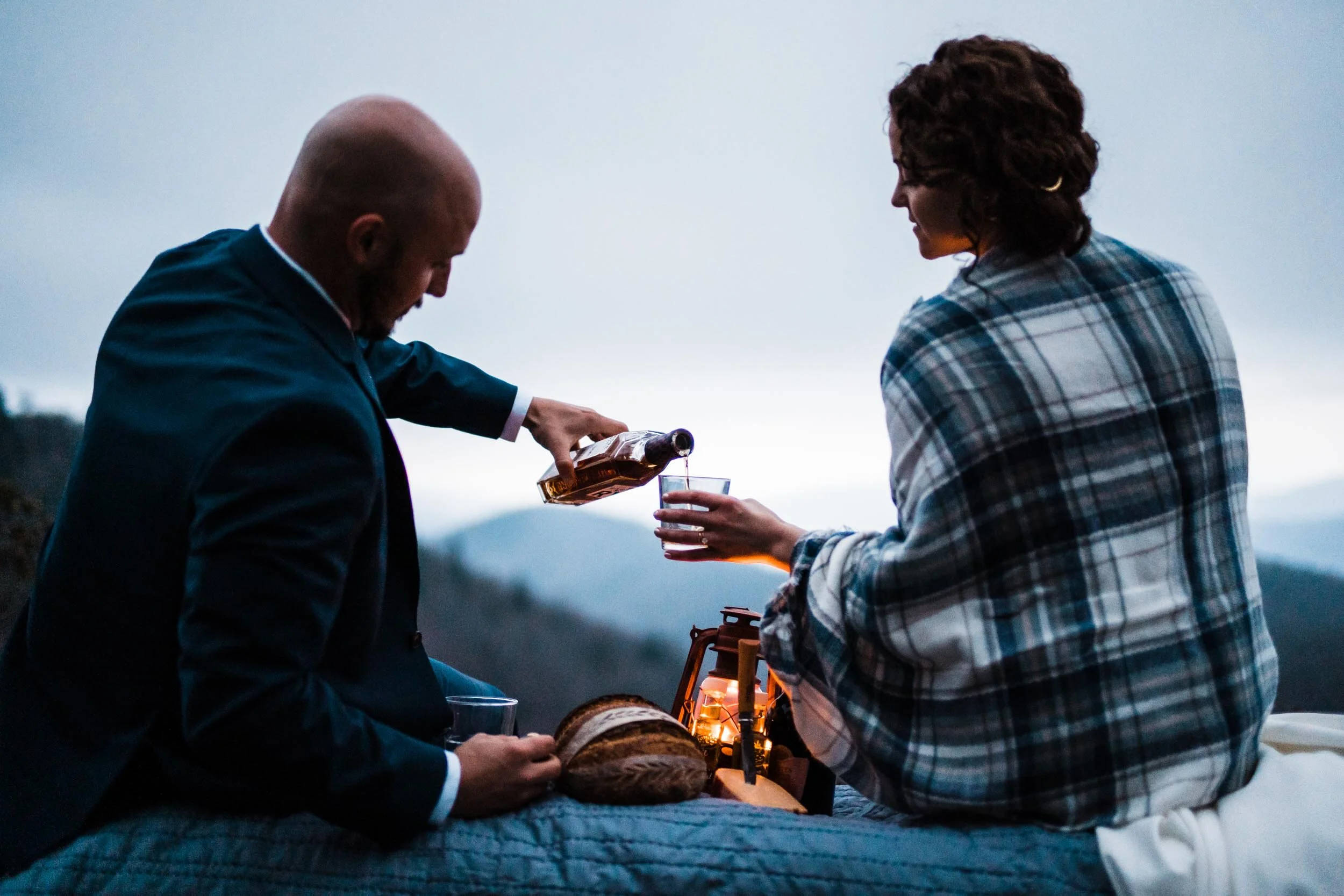 Newly married couple sharing drinks and a picnic in the mountains after sunset