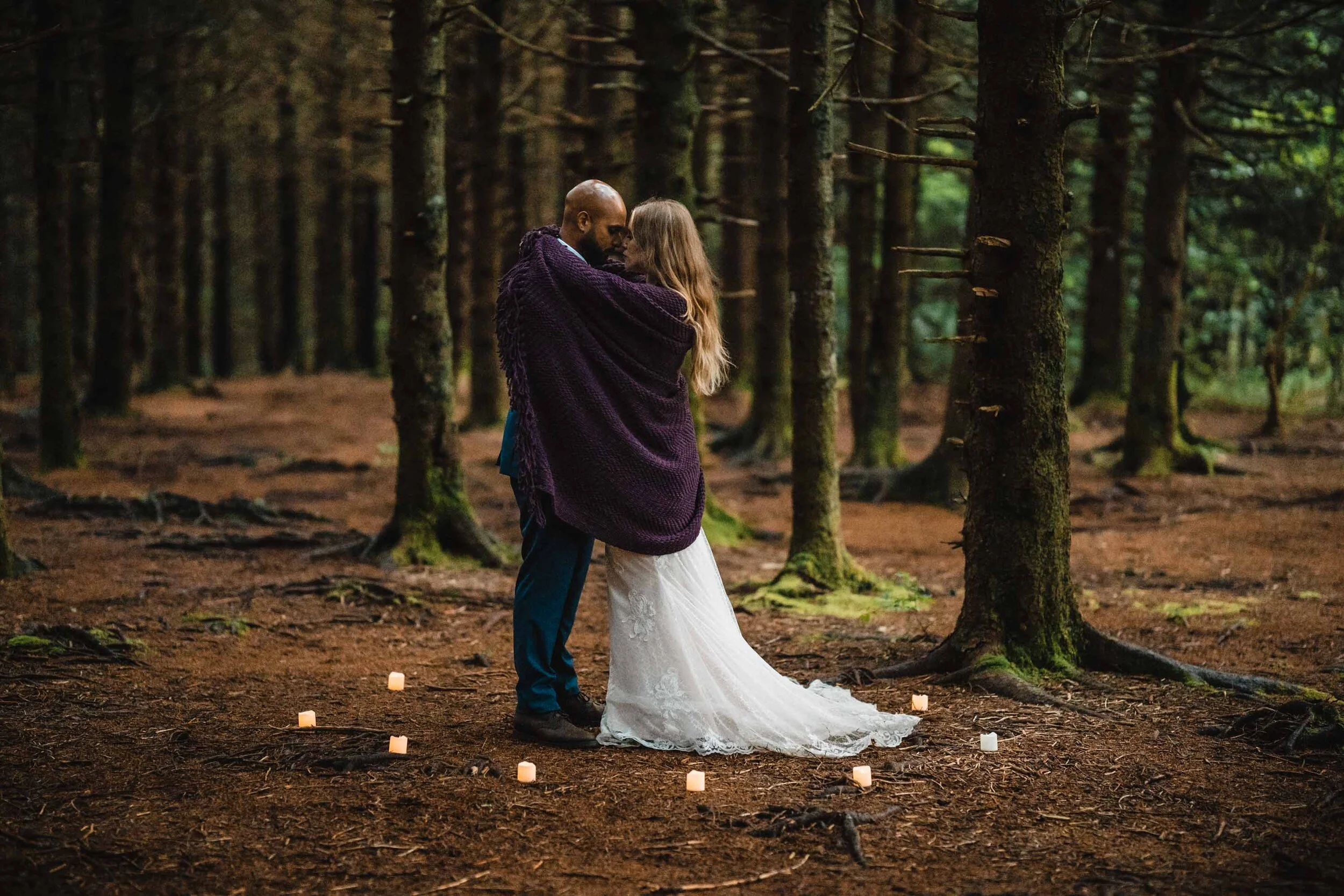 Bride and groom wrapped together in a purple shawl in a mountain forest