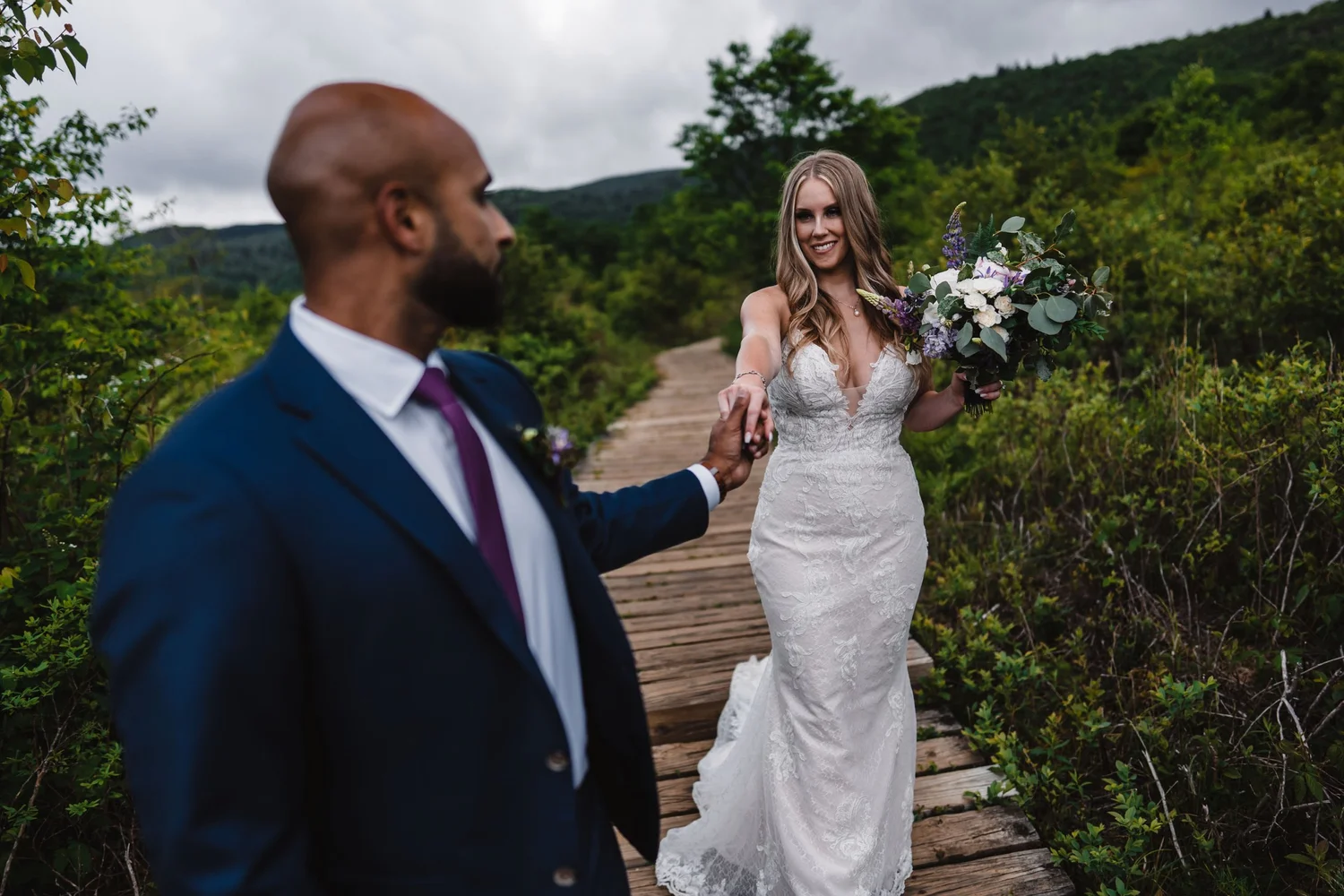 Groom leading a bride along a wooden path during a green summer wedding