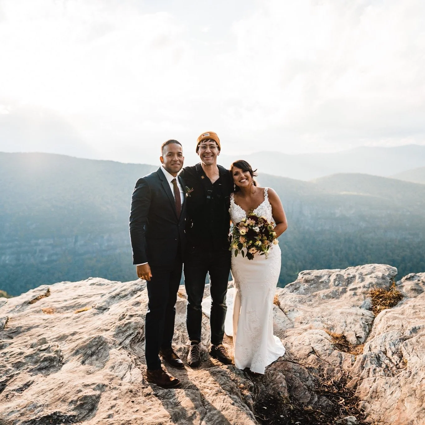 Andy pictured in a winter cap and smiling between a bride and groom at sunset.
