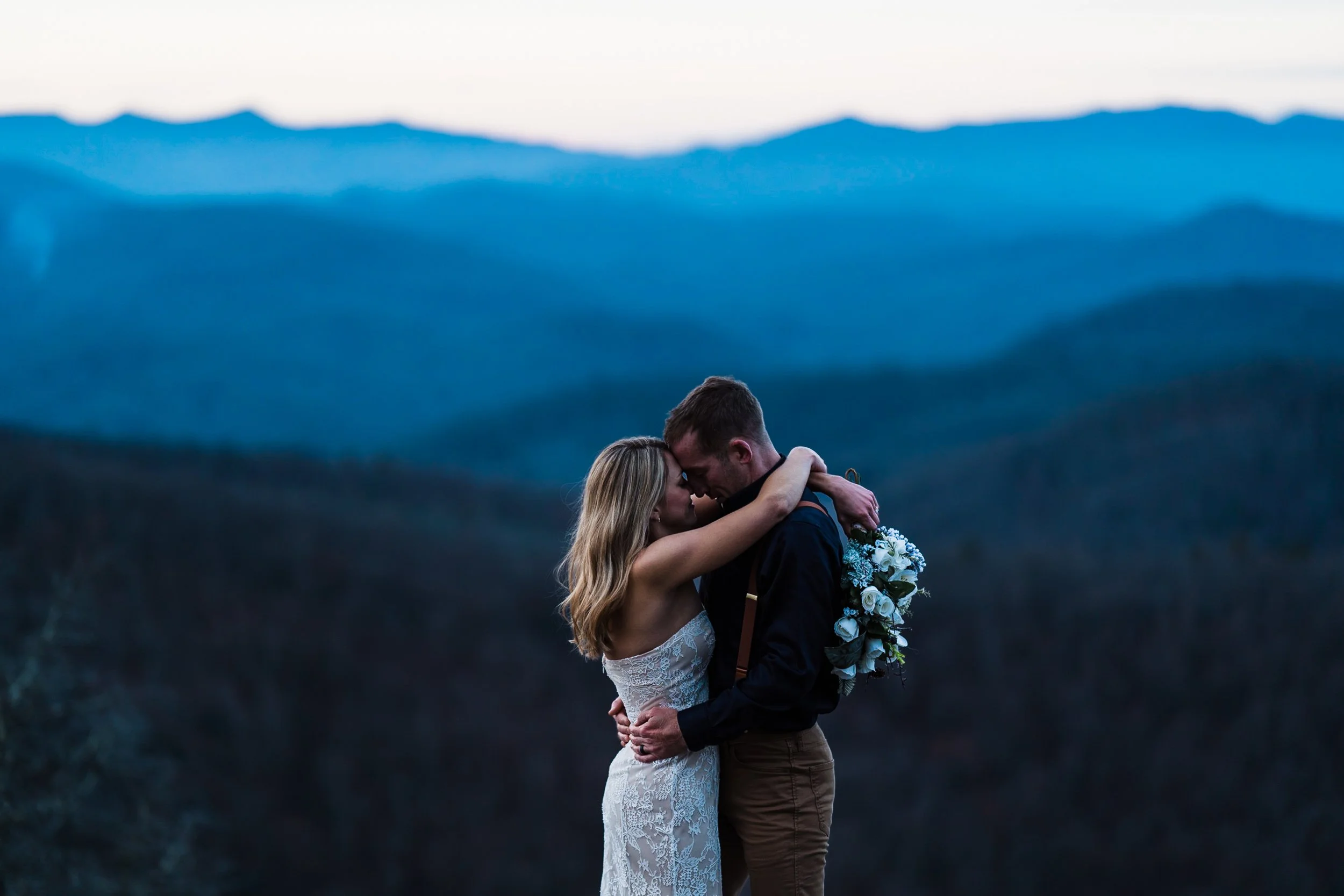 A couple embracing during their wedding at sunset with a mountain landscape in the background.