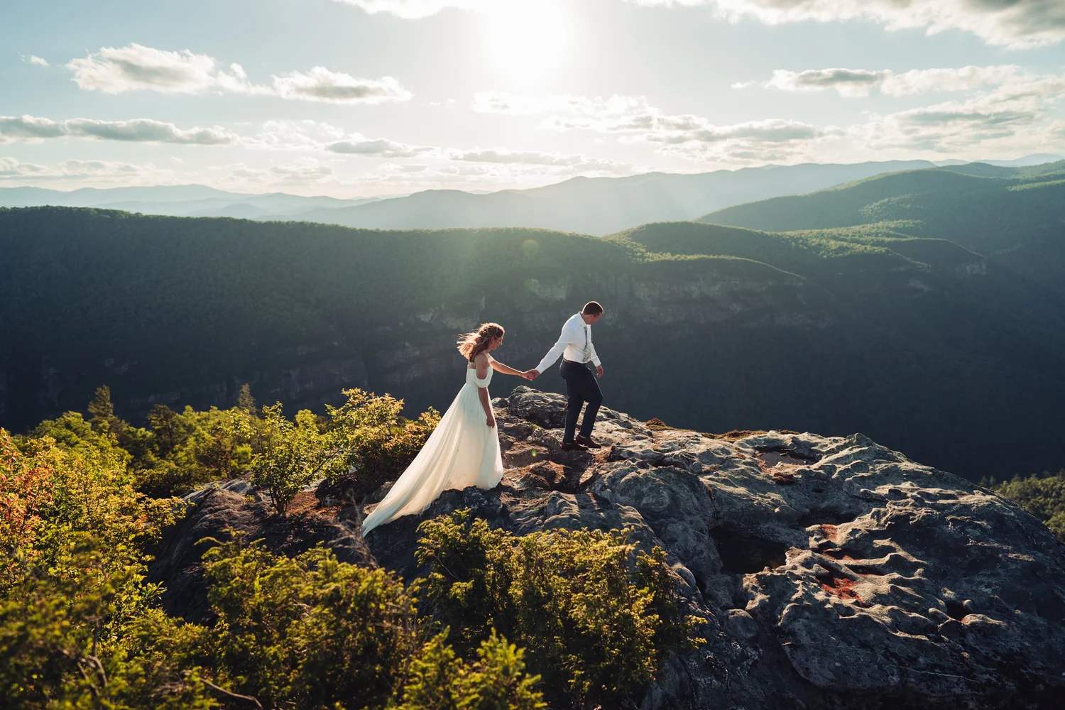Kaitlyn and Evan walking together across a rocky Linville Gorge overlook in evening light