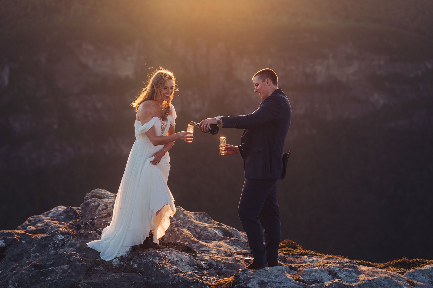 Kaitlyn and Evan pouring champagne together in warm sunset light above Linville Gorge