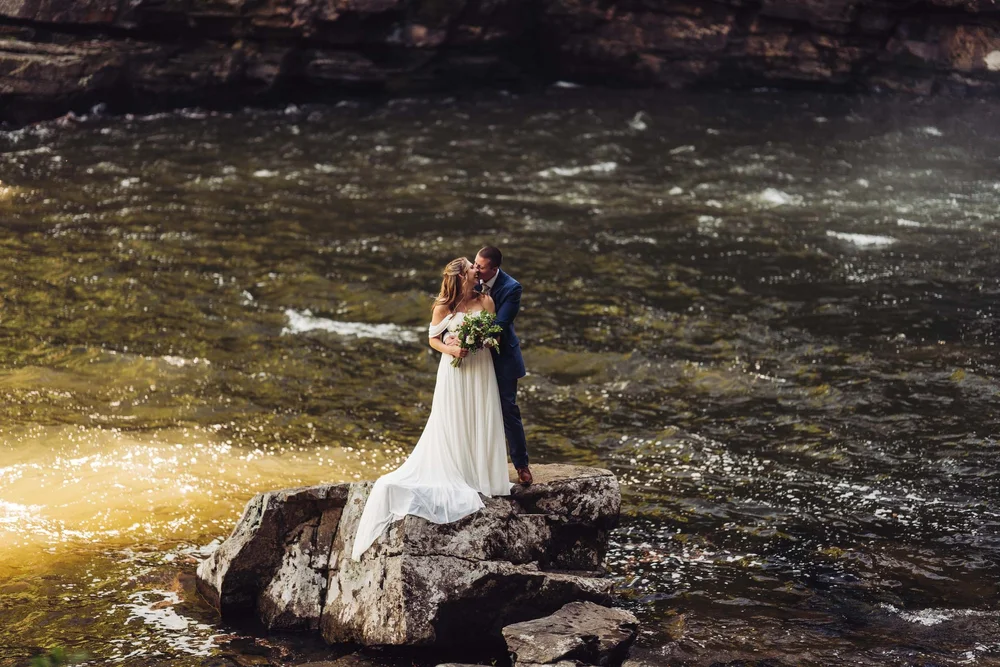 Kaitlyn and Evan standing together on a rock beside the river during their elopement