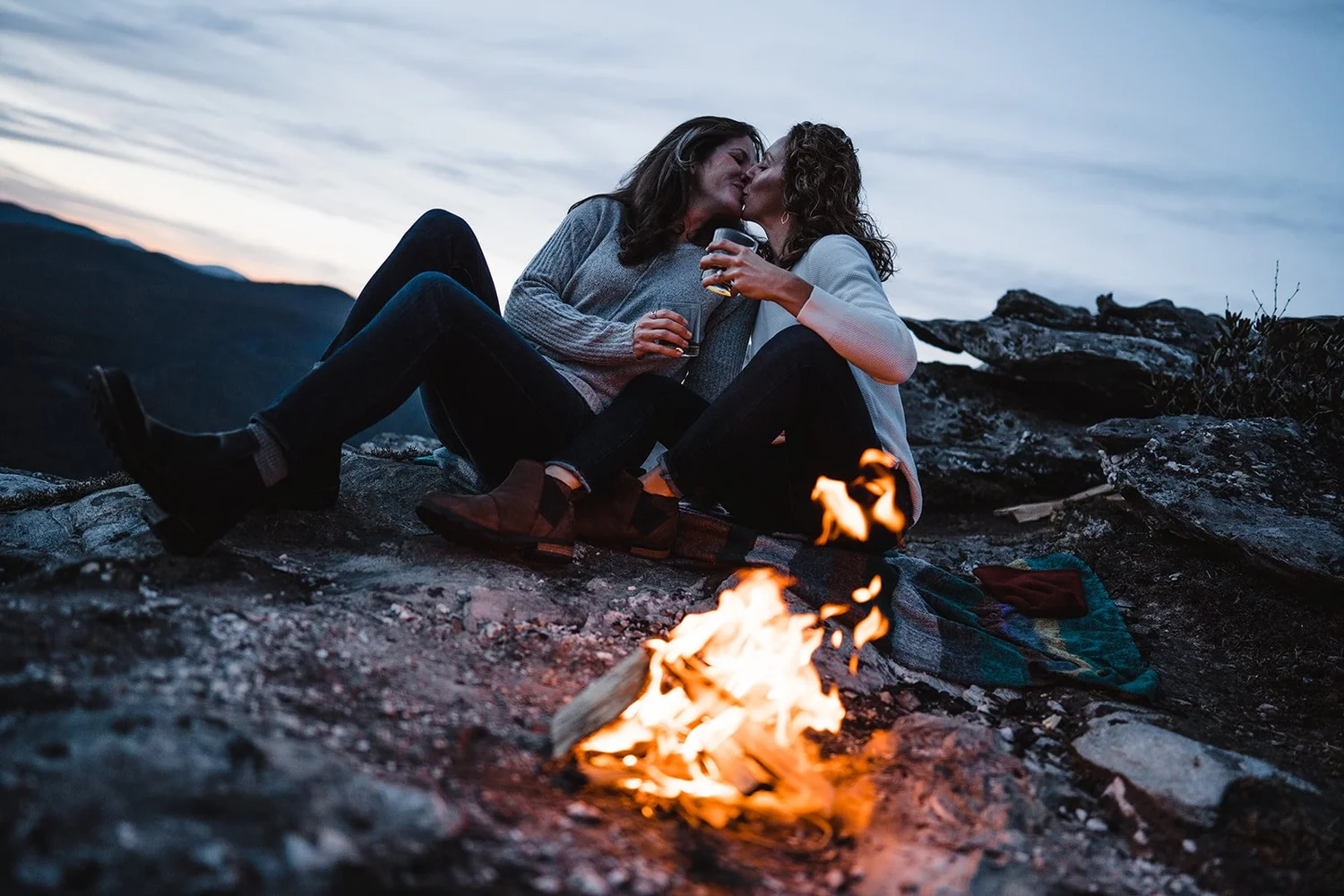 Couple kissing beside a small campfire at a mountain overlook after sunset