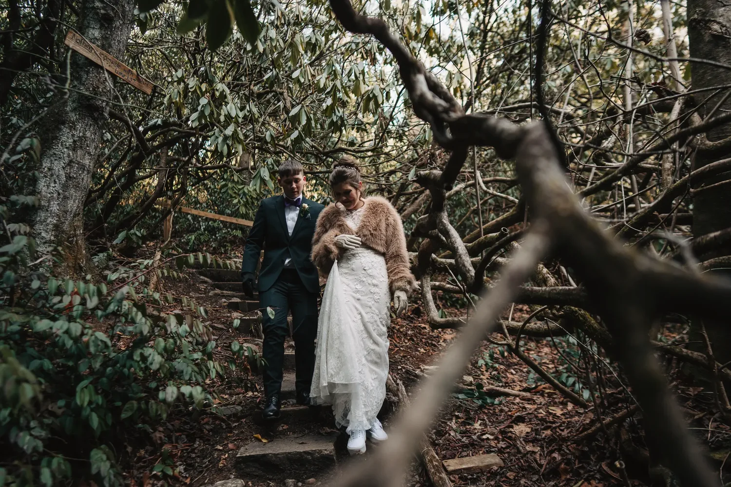 Couple in wedding attire walking together through a wooded trail