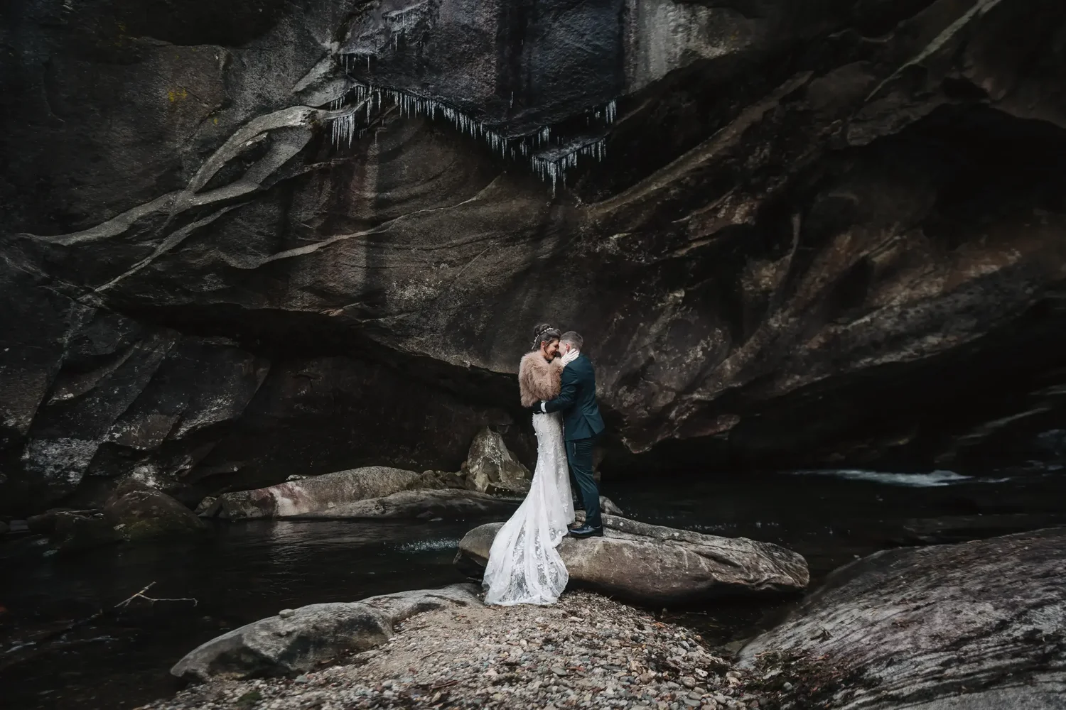 Couple embracing beneath a large rock overhang during their mountain elopement