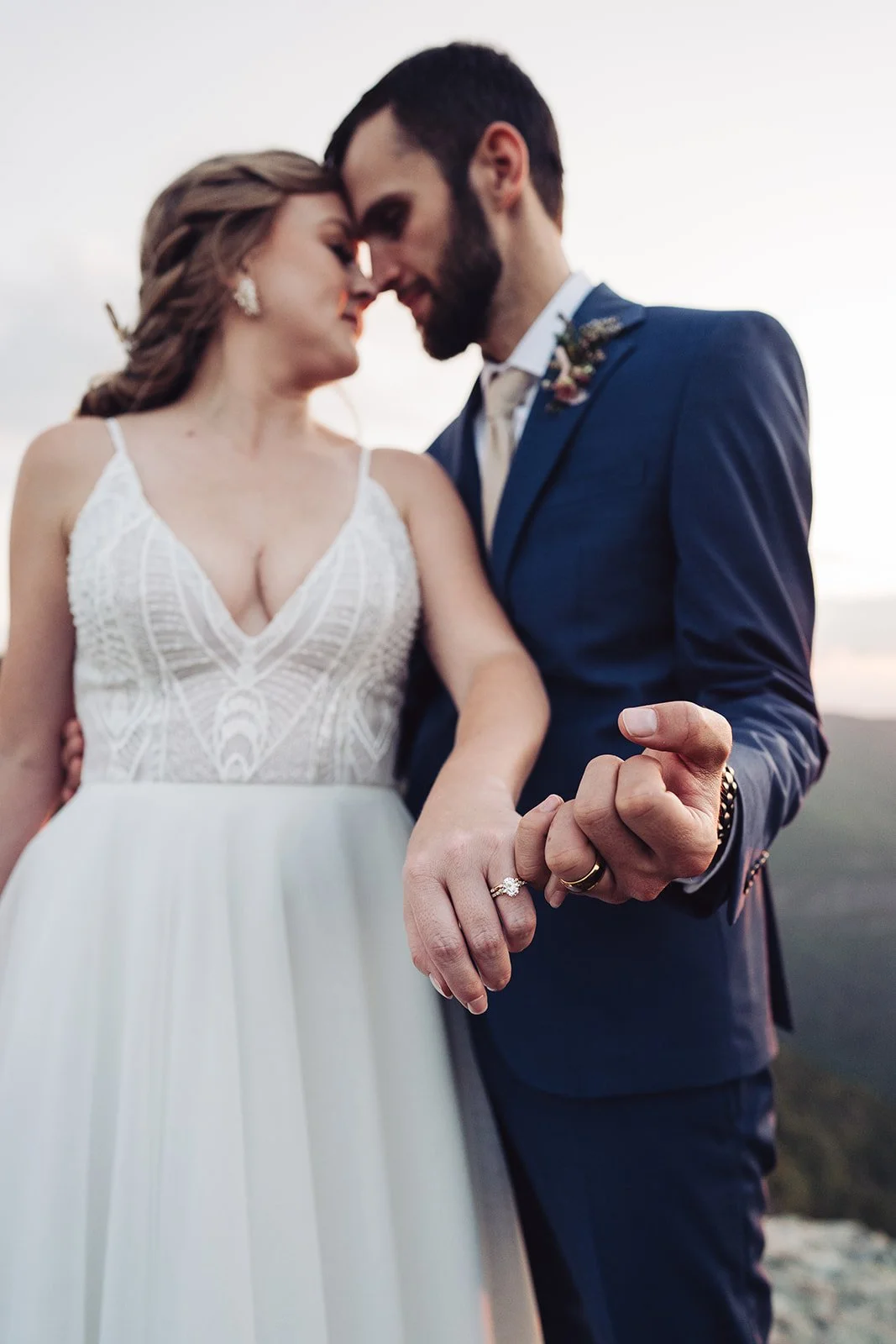 A newlywed couple standing close together, holding hands, with their foreheads touching during a sunset outdoor wedding.