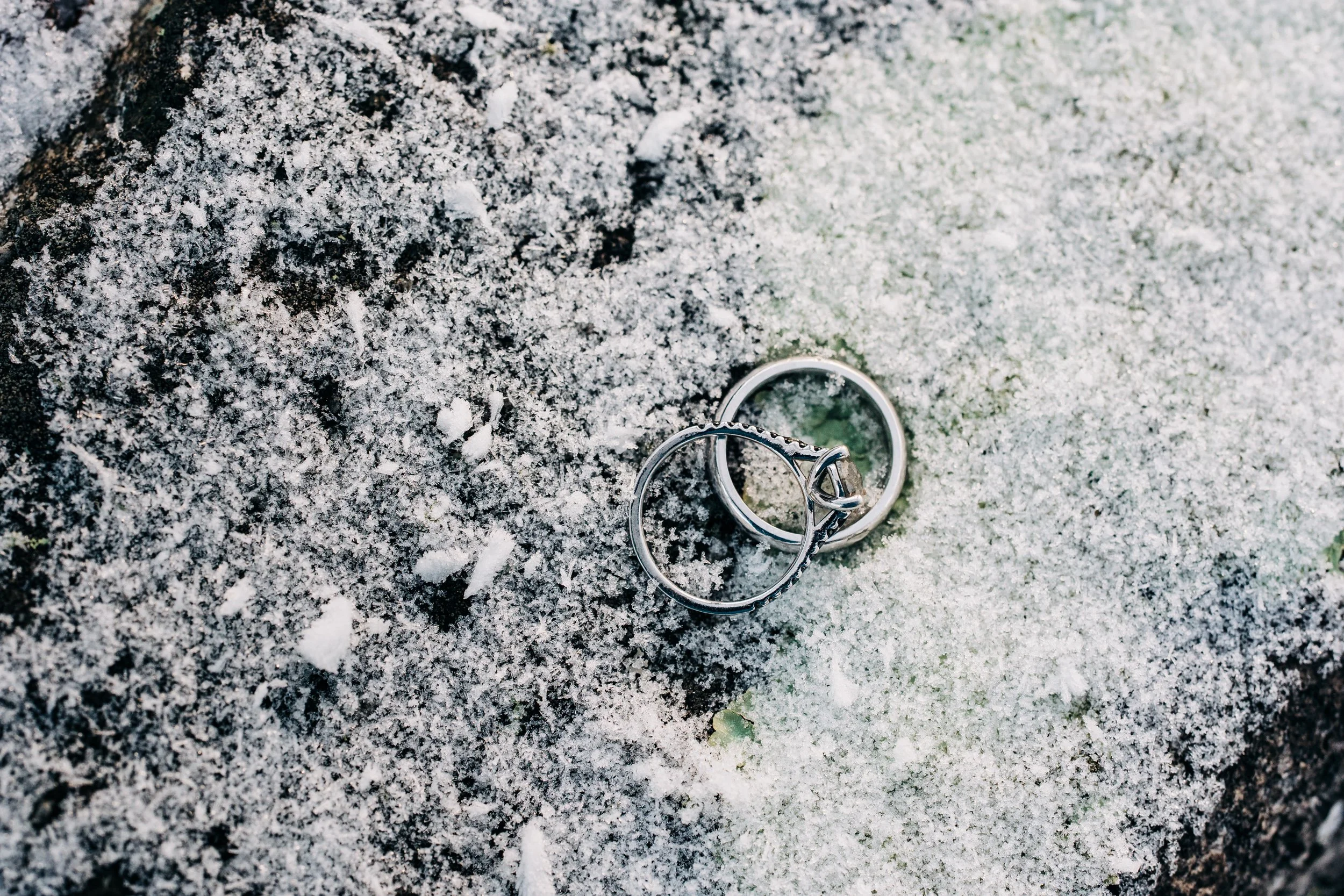 Two silver rings partially covered in snow on a dark, textured surface.