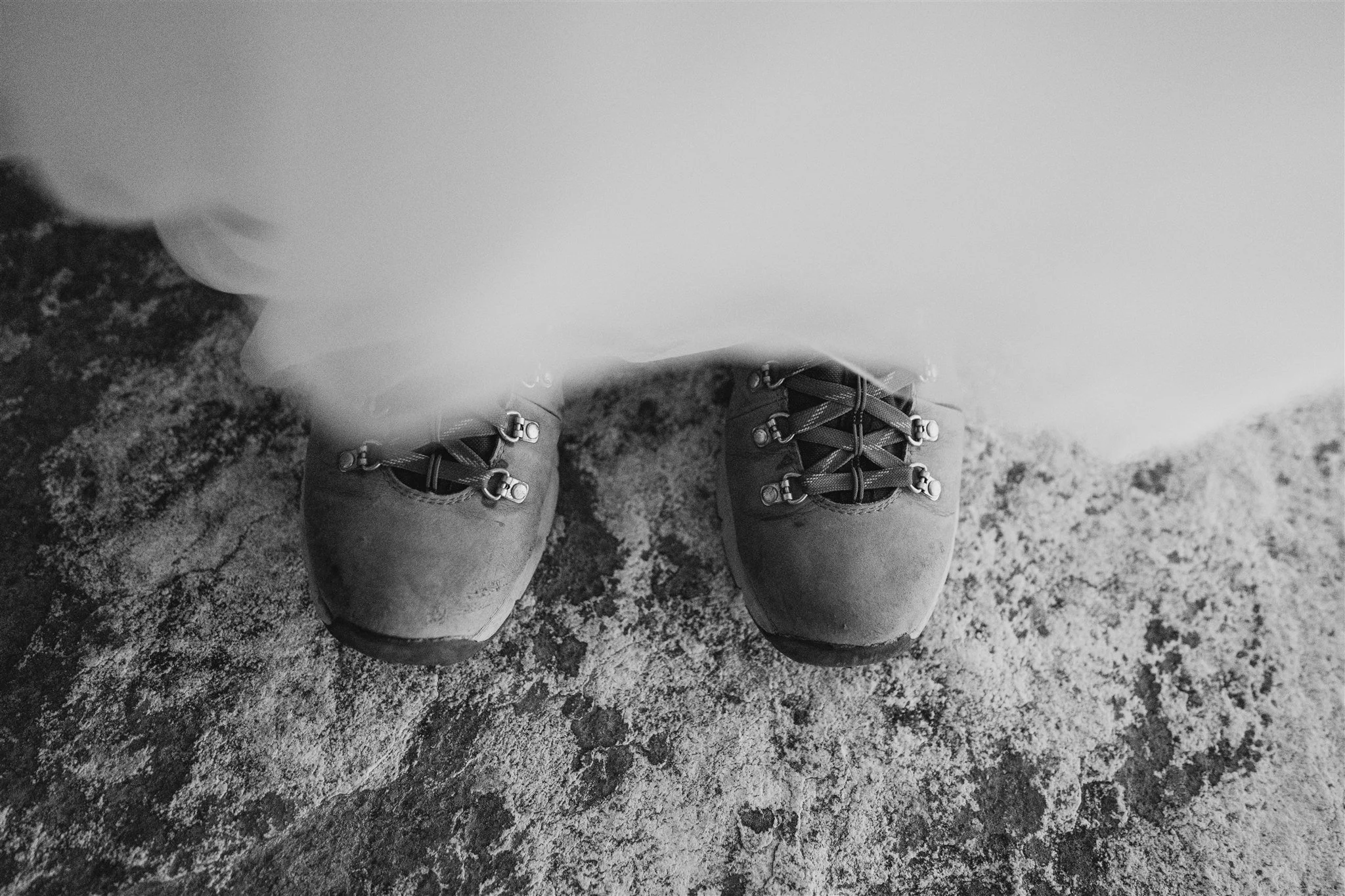 A person wearing hiking boots standing on a rugged, rocky surface.
