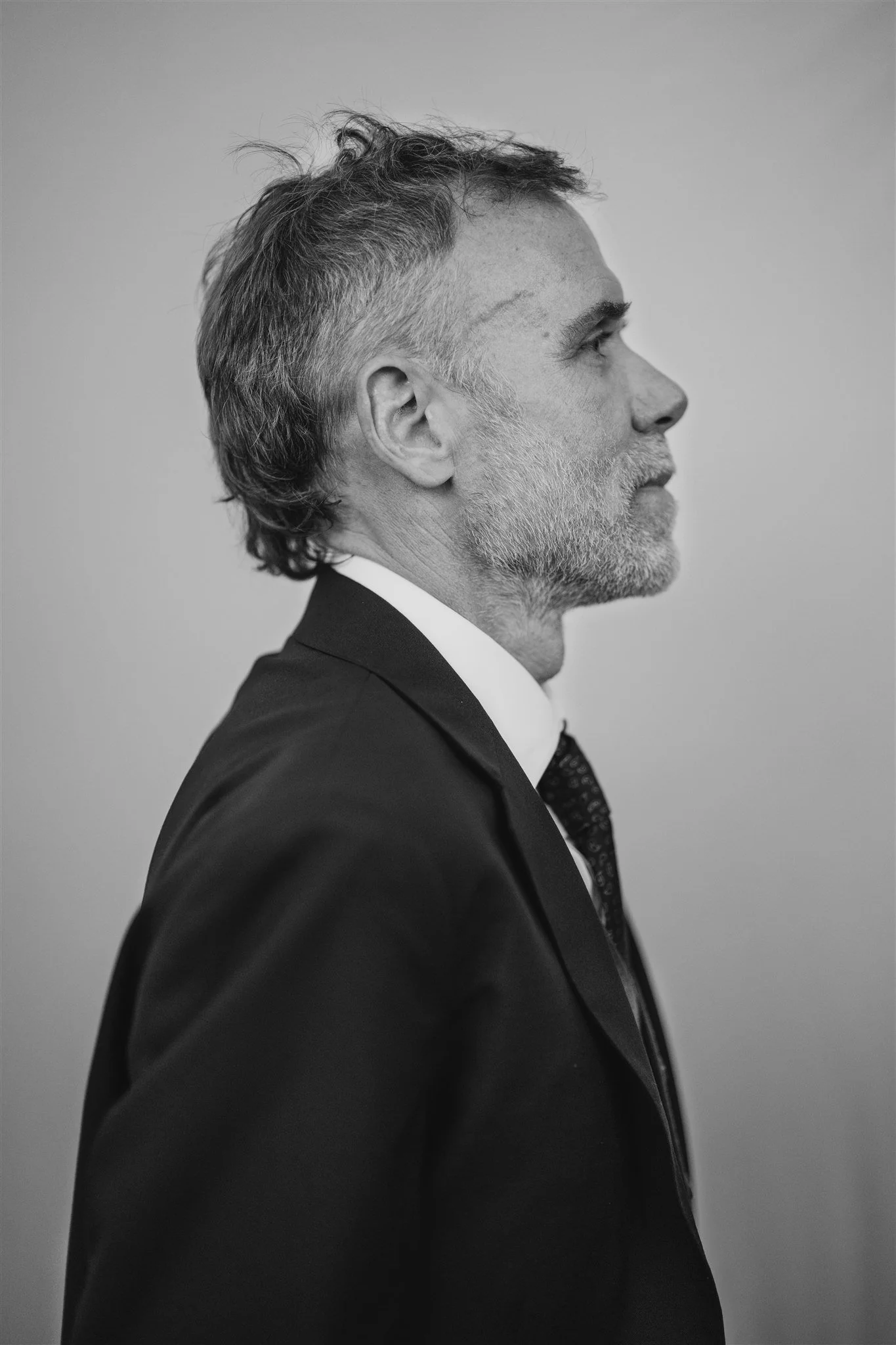 Profile side view of a mature man with gray hair and beard, wearing a suit and tie, in black and white.