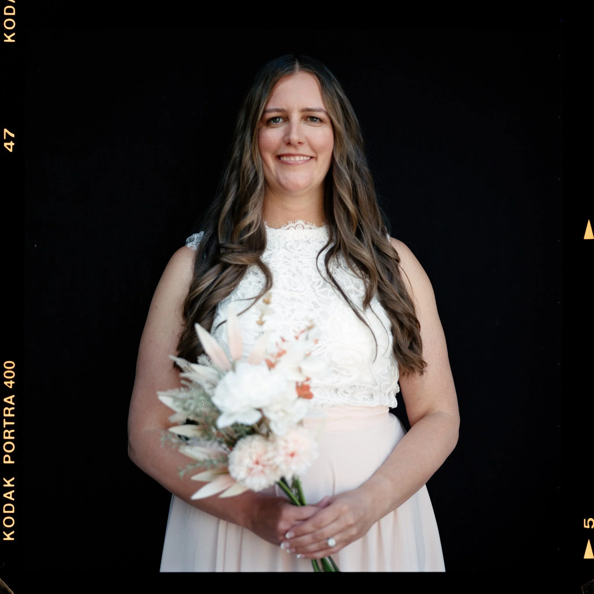 A woman in a white lace dress holding a bouquet of white flowers against a black background.
