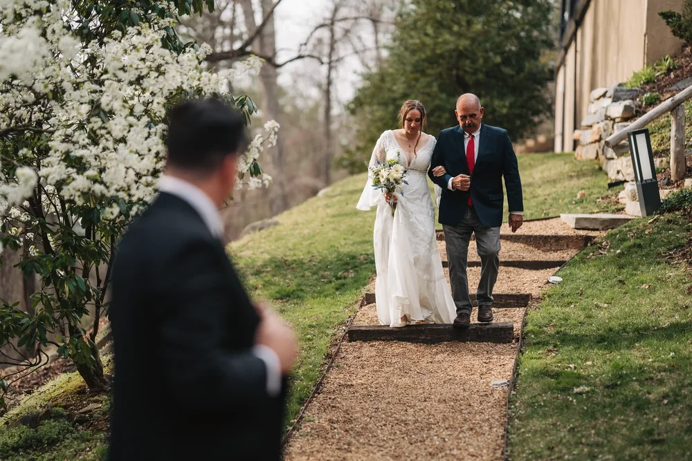 Bride walking toward her partner with her father during an outdoor wedding