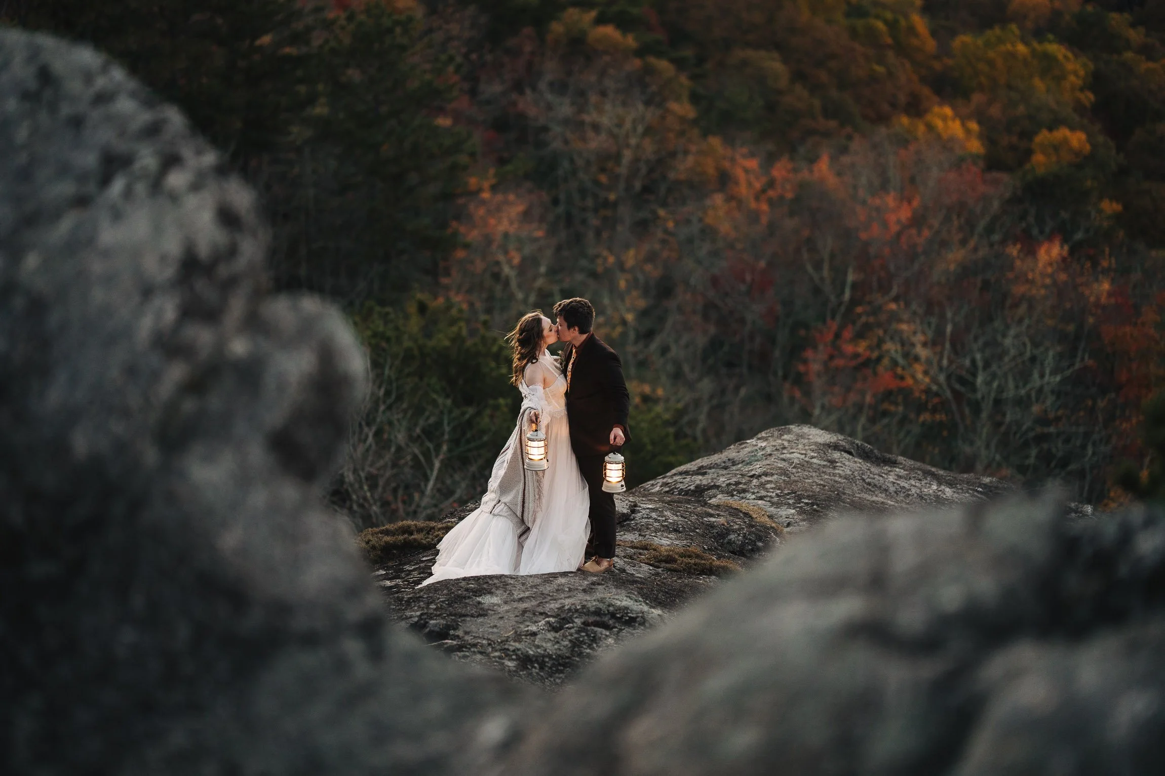 Couple embracing on a mountain trail at sunset, surrounded by spring greenery and warm evening light.