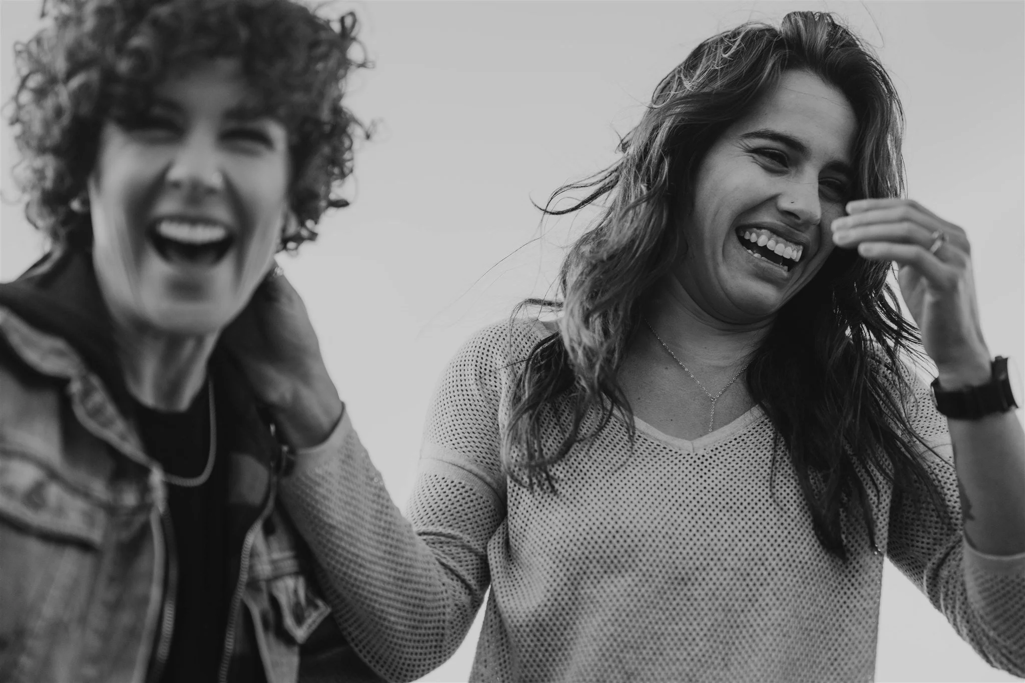 Two women laughing and smiling, one with curly hair and the other with wavy hair, in black and white.