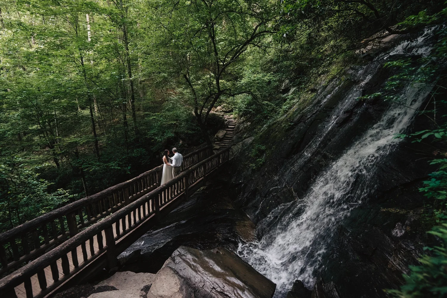 Couple standing together on a forest bridge beside a waterfall in Western North Carolina
