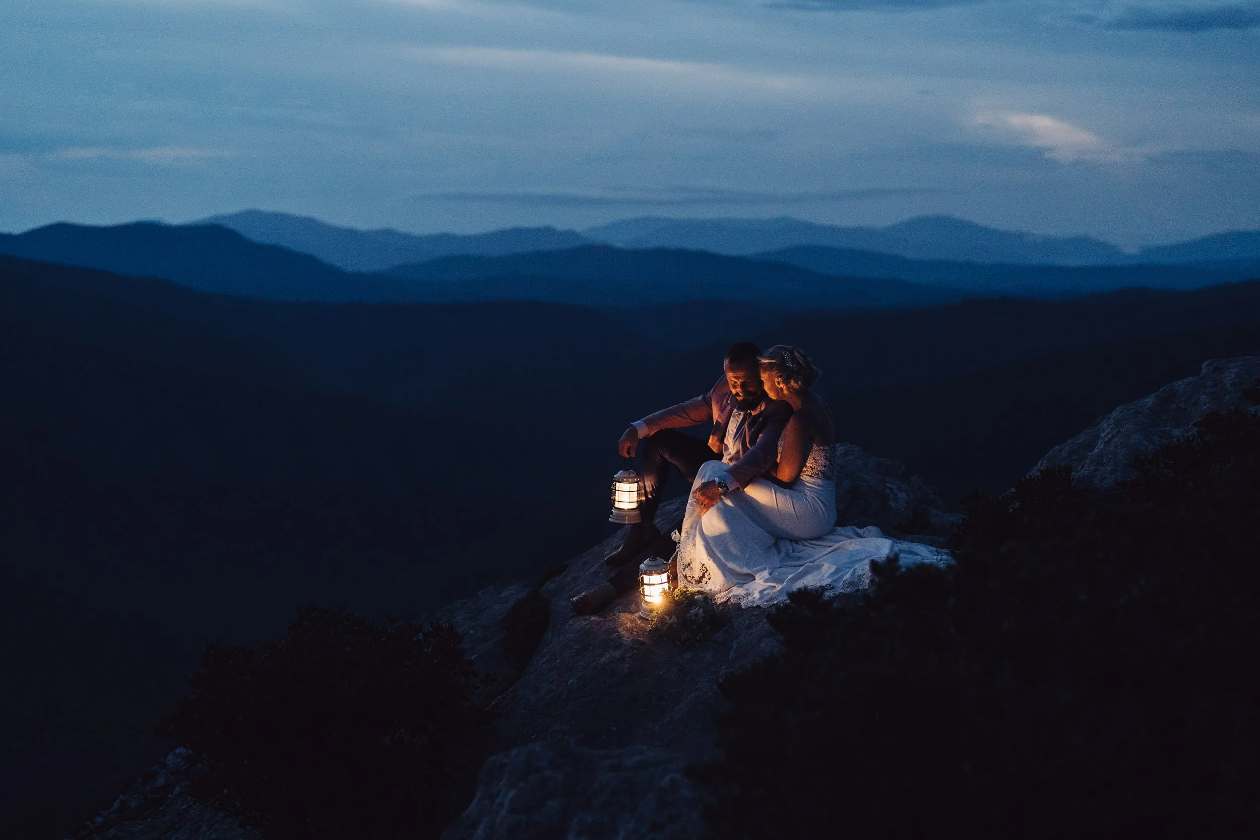 Couple sitting with lanterns on a mountain at dusk