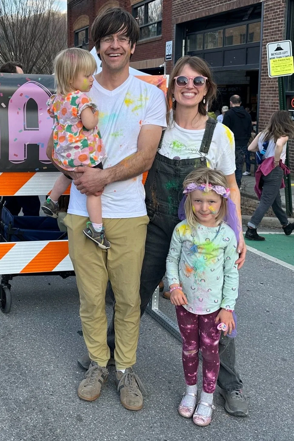 Family covered in colorful powder at an outdoor street festival.
