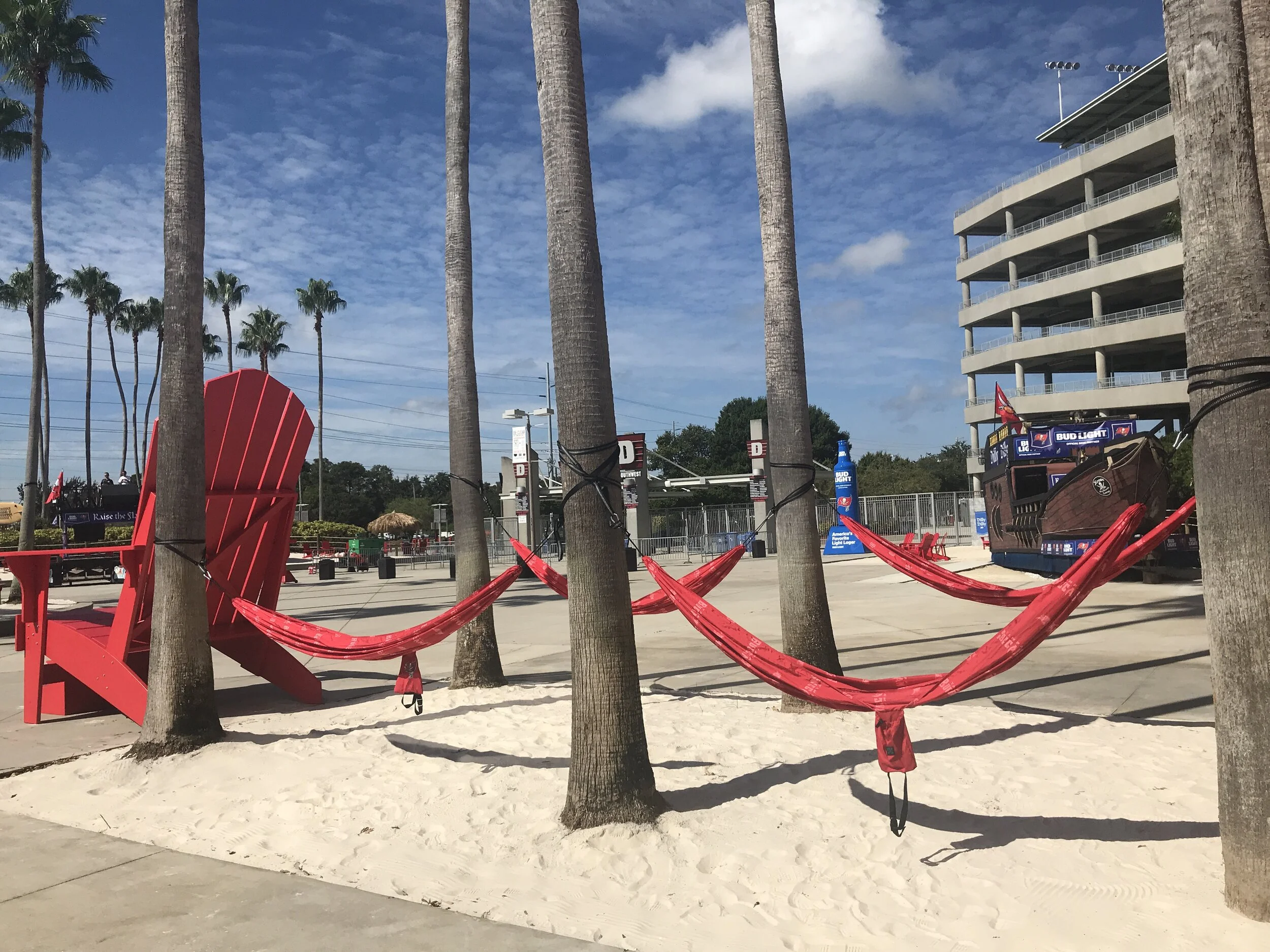 Hamcocks hang from palm trees with sand under them.