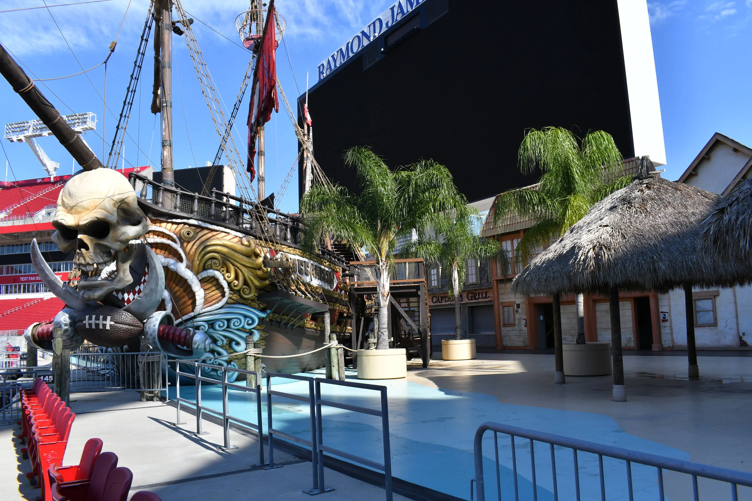 A mast and front of a pirate ship is seen outside Buccaneer Cove with palm trees and grass umbrellas..