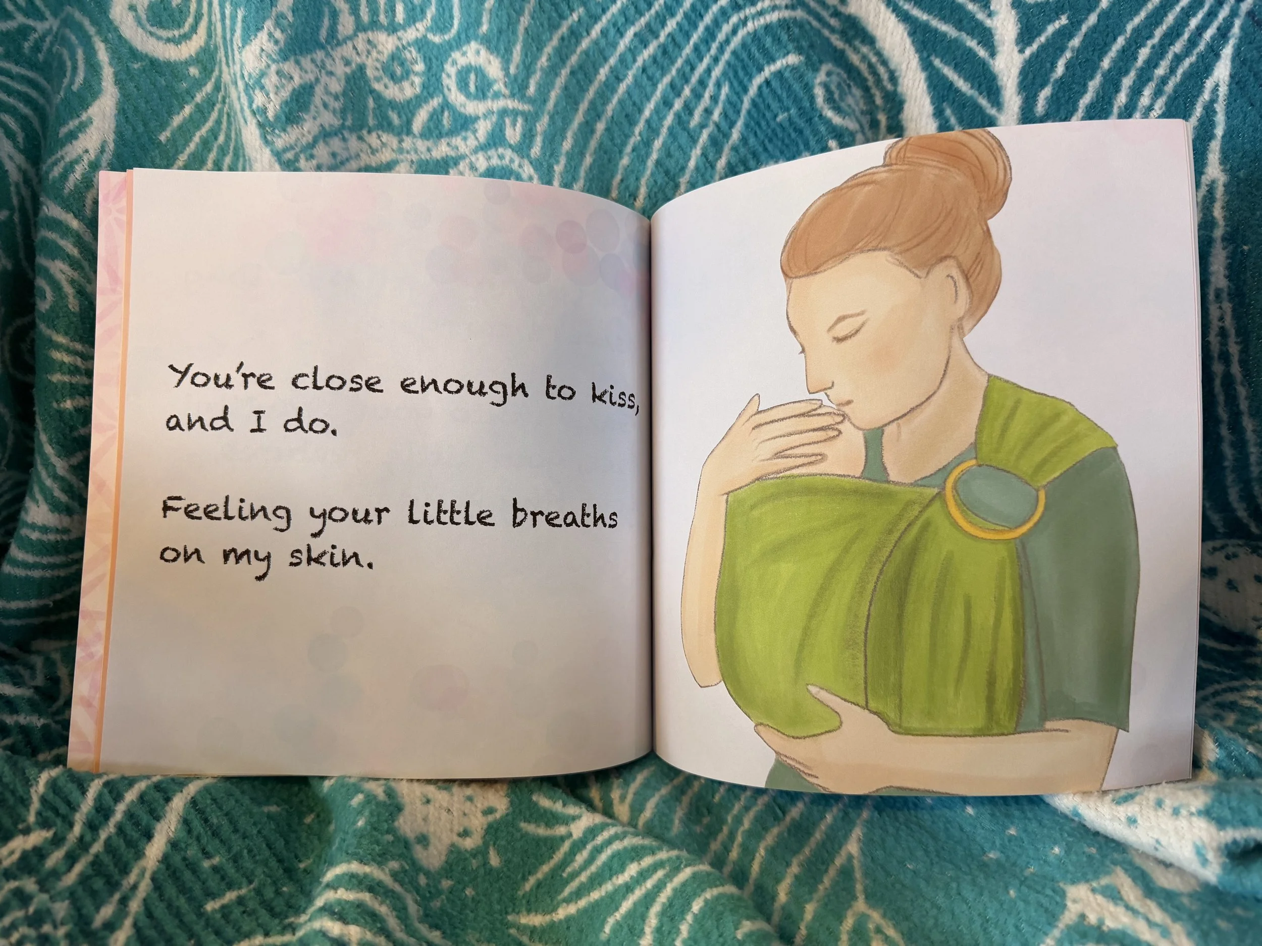 An illustration of a woman with red hair in a bun wearing a green ring sling with golden rings, holding her hand to her baby's head, looking down lovingly.