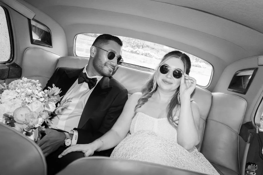 Newlywed couple in black tie riding together in a vintage car.