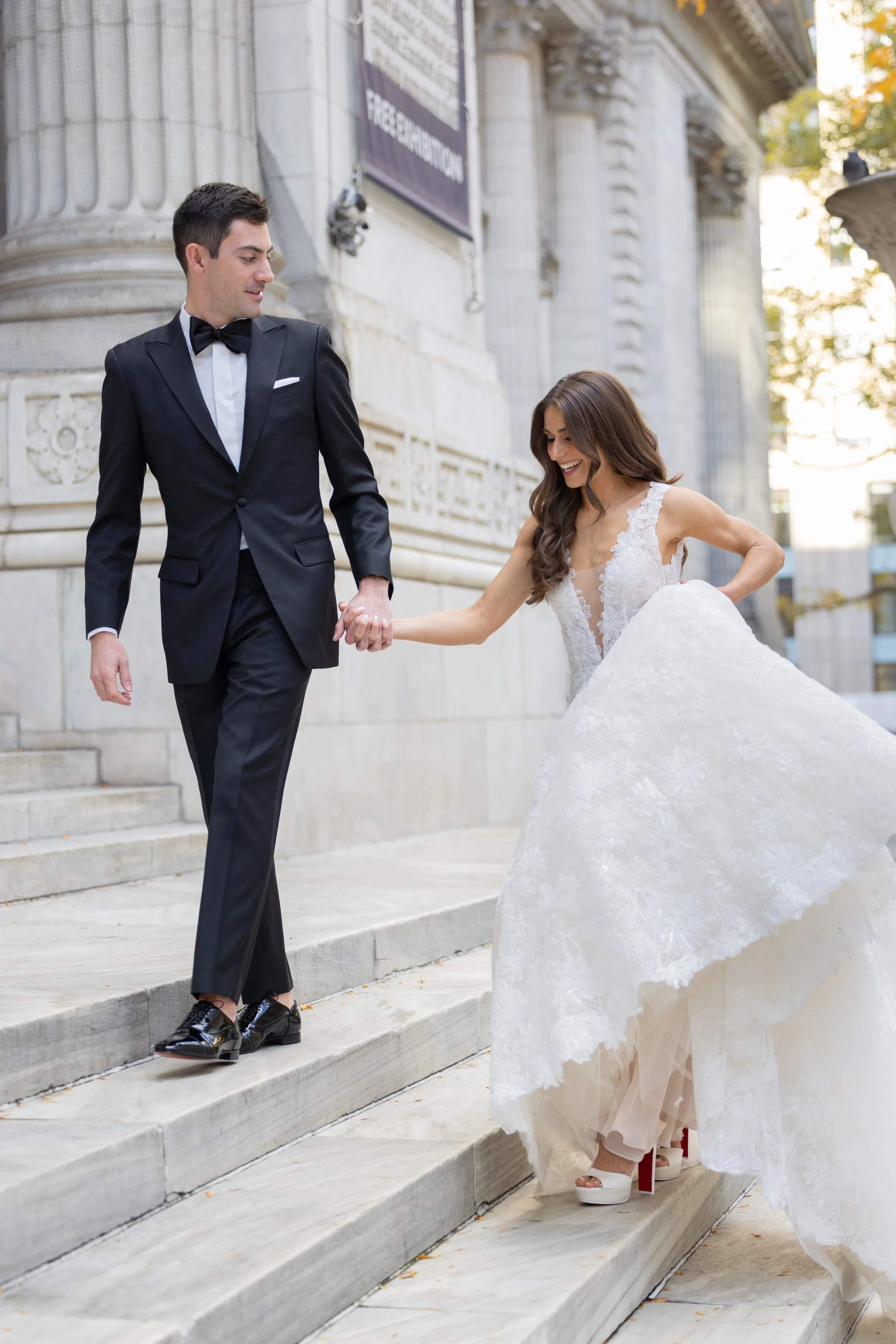 Bride and groom in black tie walking together on the steps of a New York landmark.