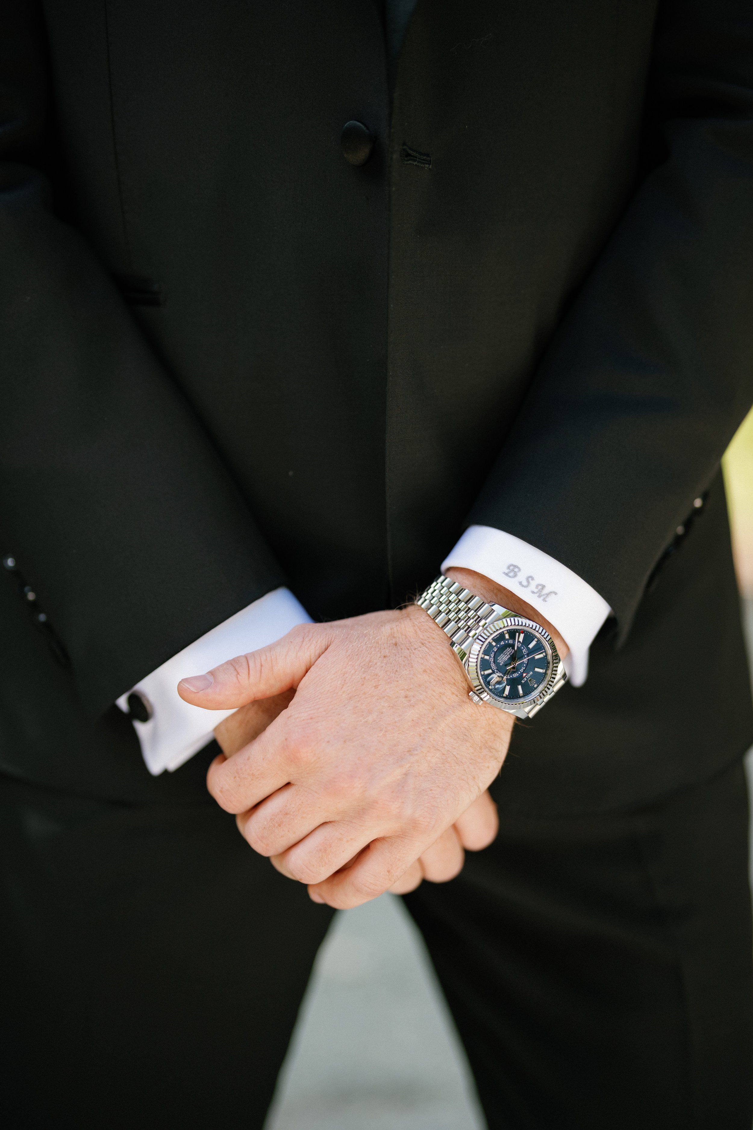 Close-up of a custom black tuxedo, monogrammed cuff and watch.