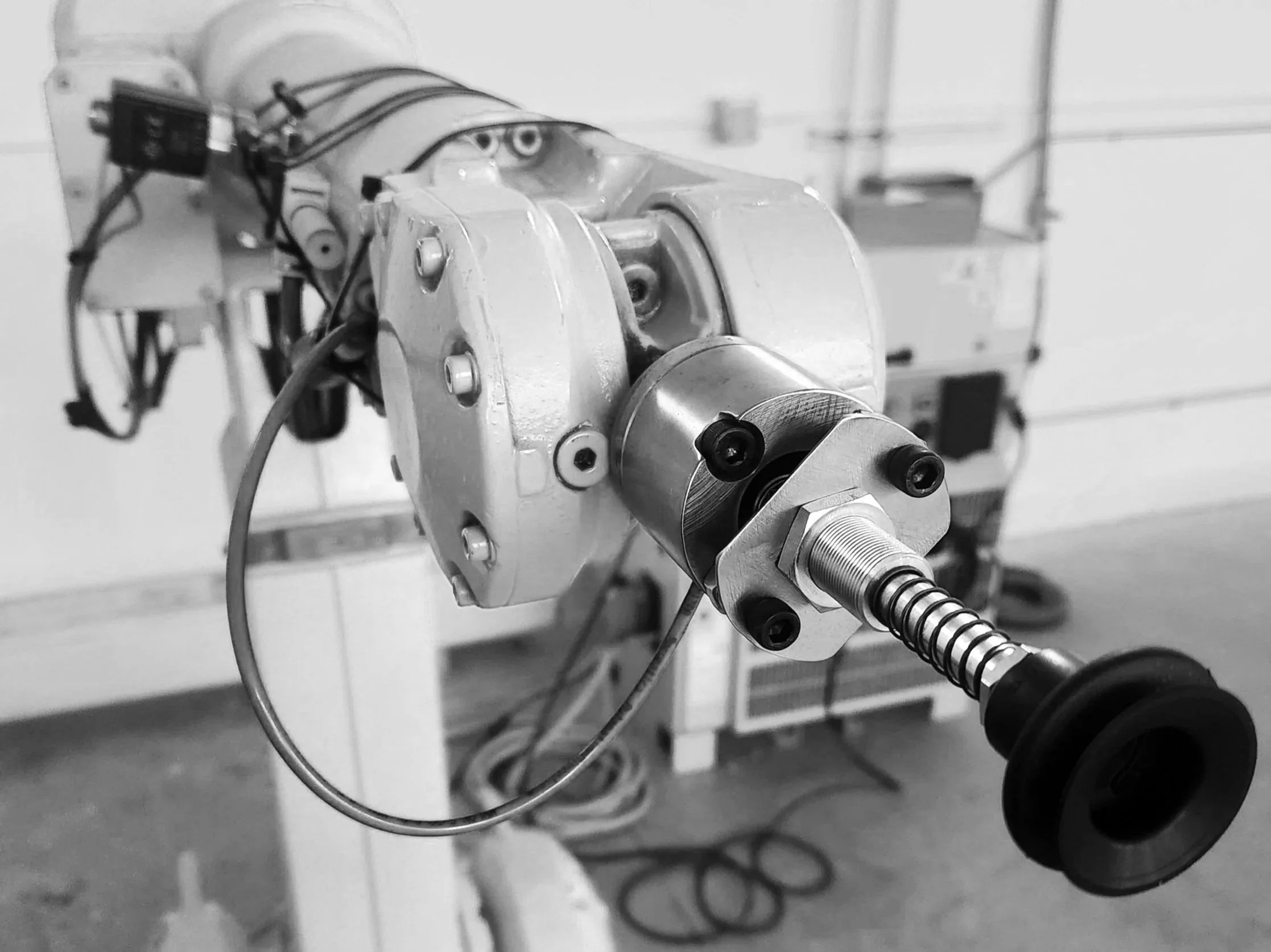 Close-up of an orange ABB industrial robotic arm with a suction cup end-effector (EoAT) and wiring in a workshop setting.