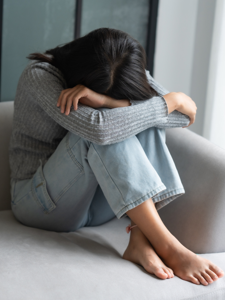 Woman sitting alone on a couch with her head down, appearing emotionally distressed