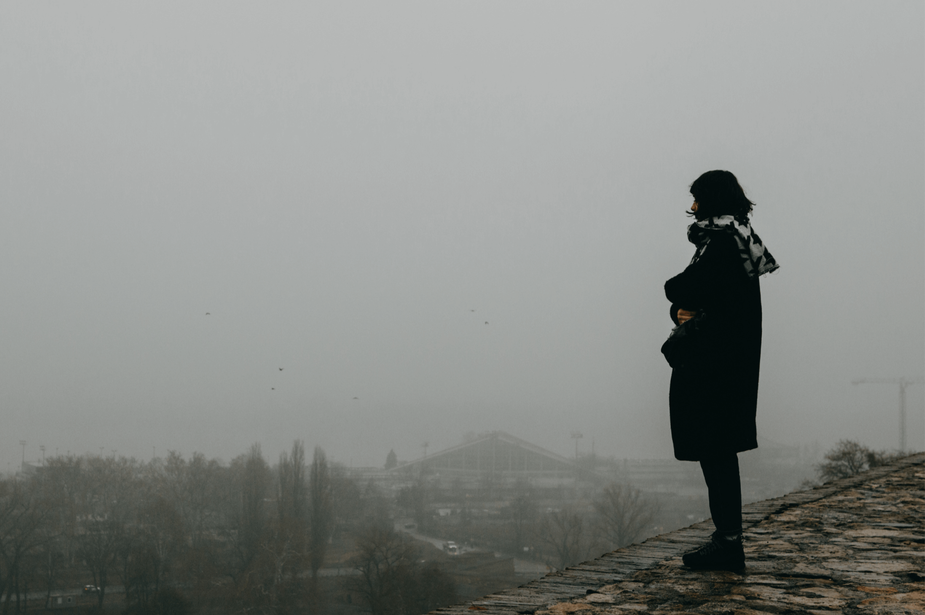 Solitary figure overlooking a fog-covered city, conveying homesickness, uncertainty, and the quiet grief of leaving home