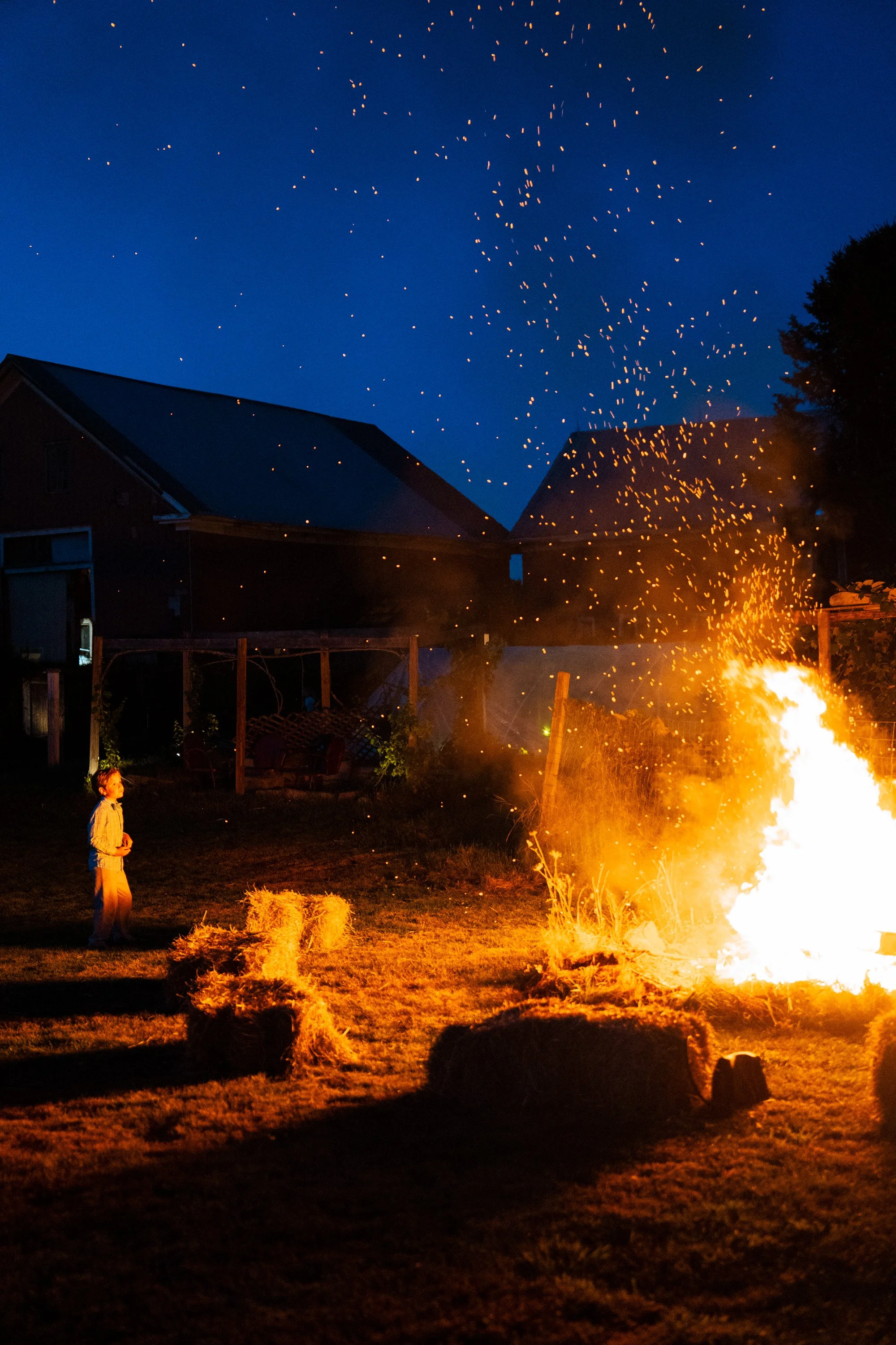 Photo of a bonfire with embers floating into the blue night sky.