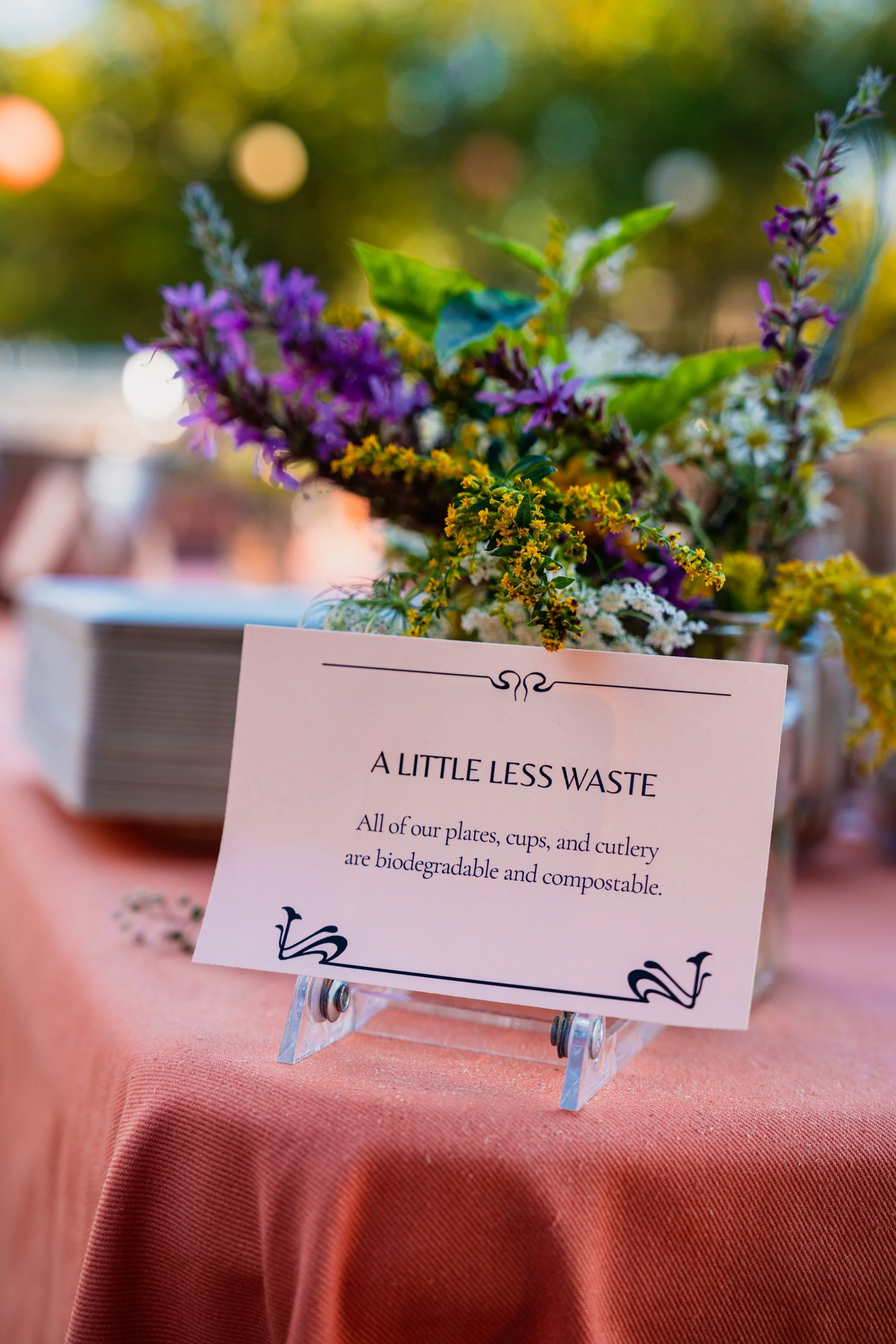 Photo of a card propped up on a table outdoors with some purple and yellow flowers behind it.