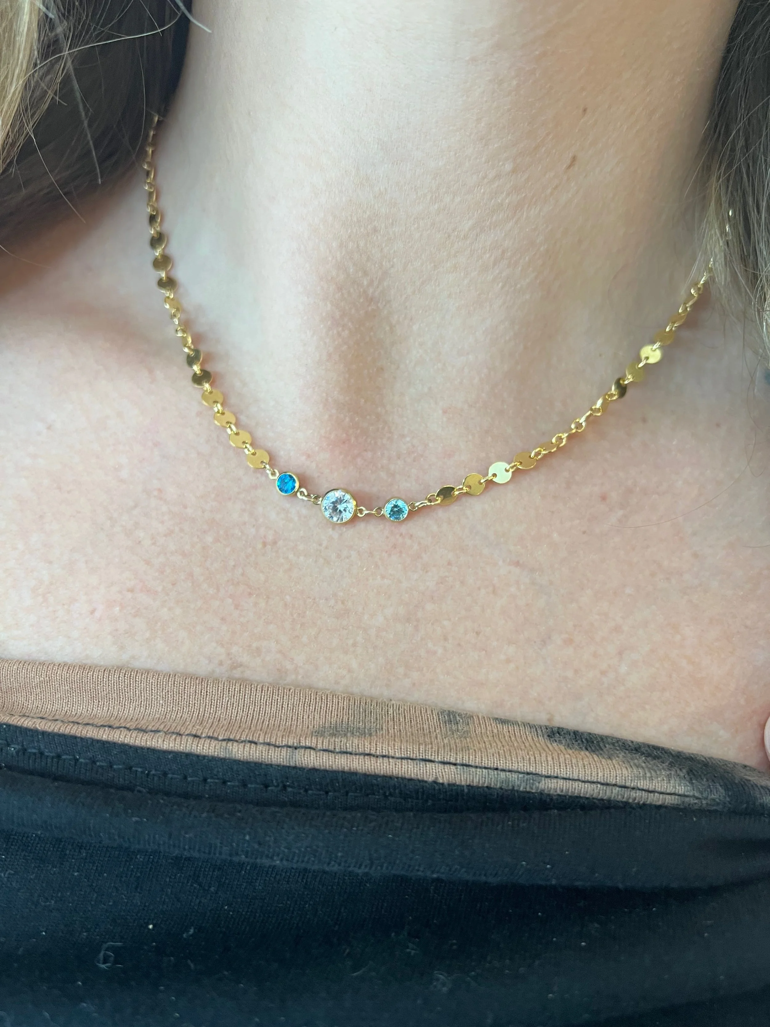 Gold chain necklace with blue gemstones on a woman's neck.