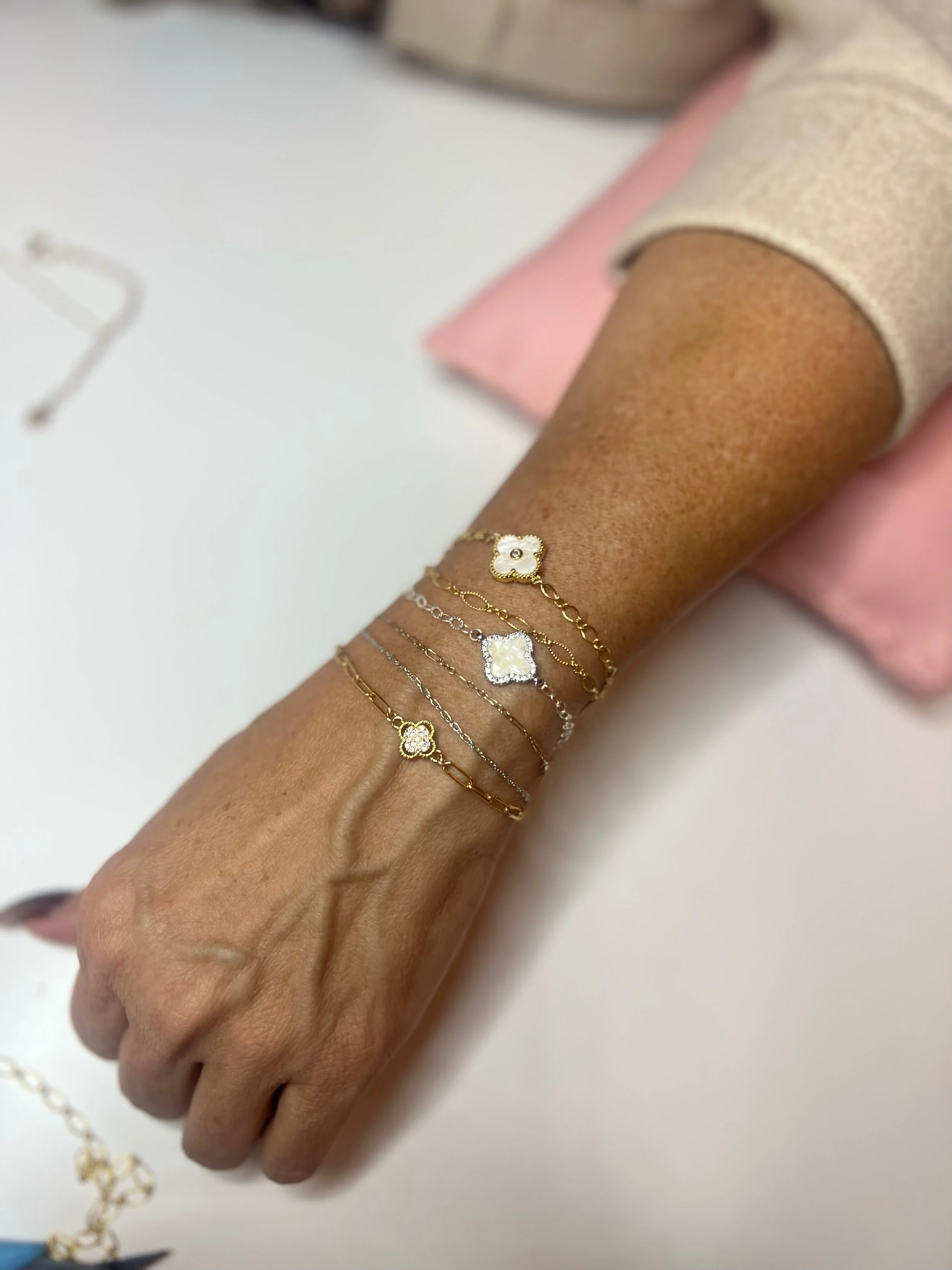 Person wearing multiple gold and silver chain bracelets with floral and geometric charms on wrist.