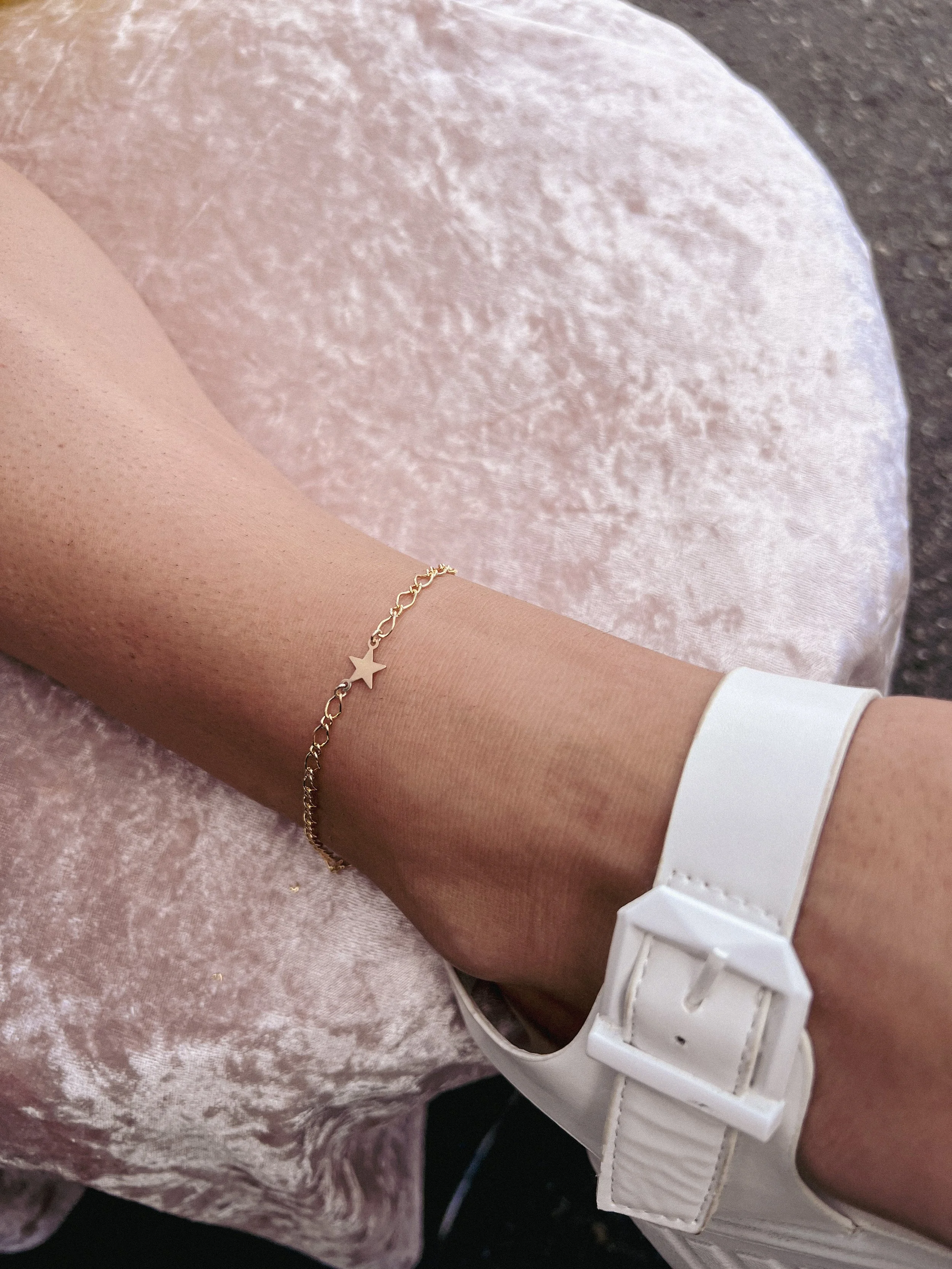 Person wearing a white shoe and a gold star bracelet, resting on a light pink fabric surface.
