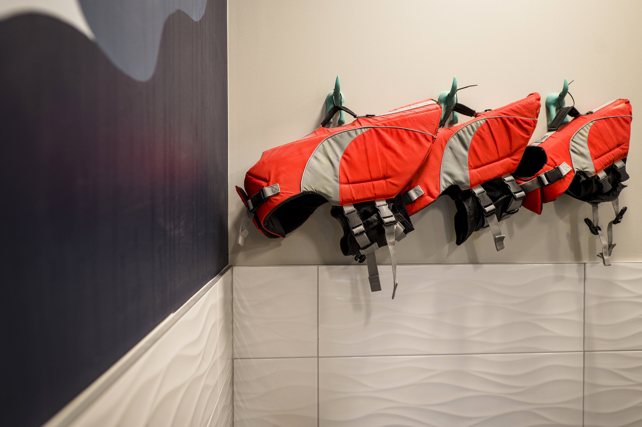Three red life jackets hanging on hooks against a wall.
